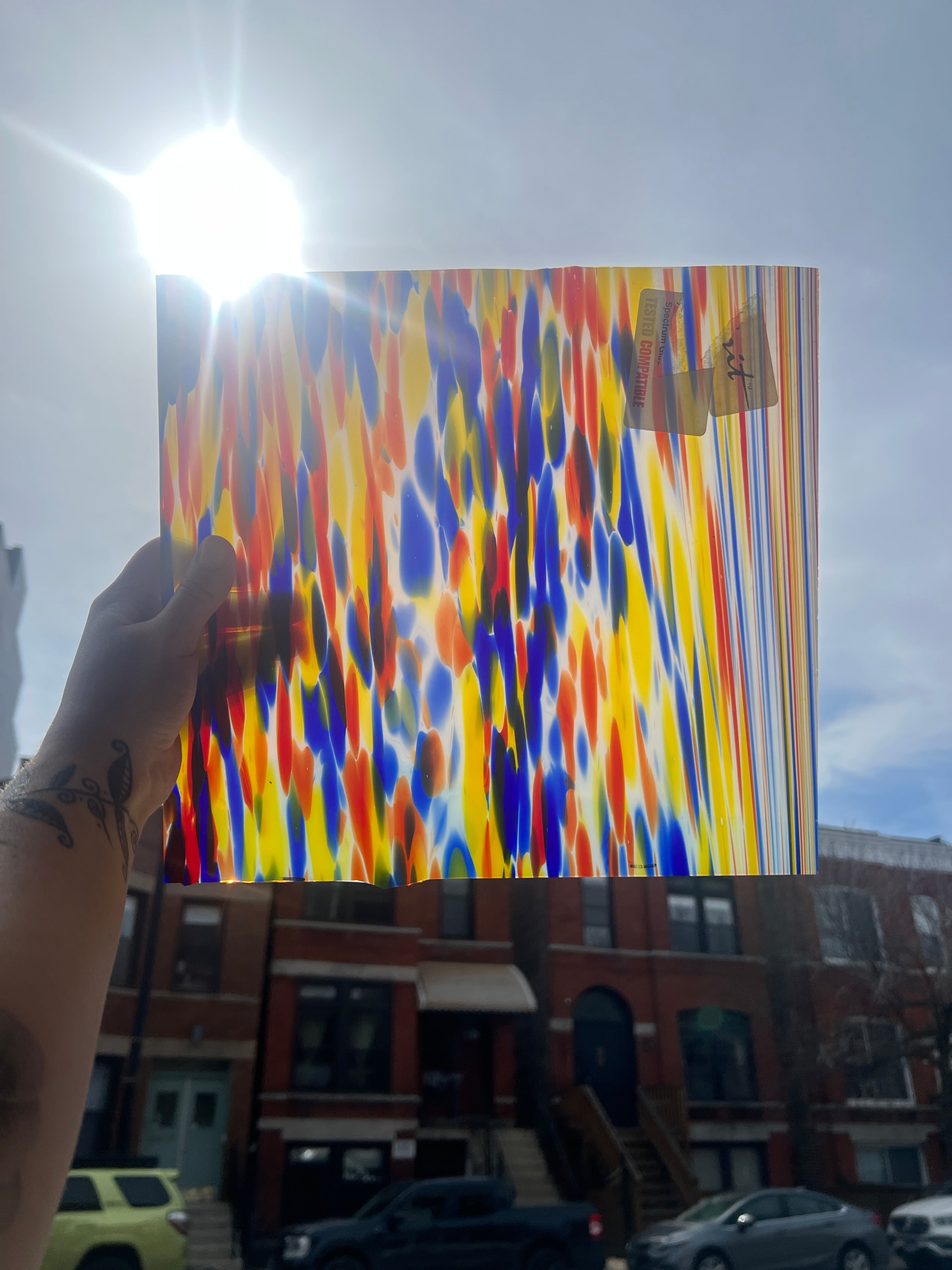 Colorful piece of stained glass held up against a cityscape with buildings and cars.