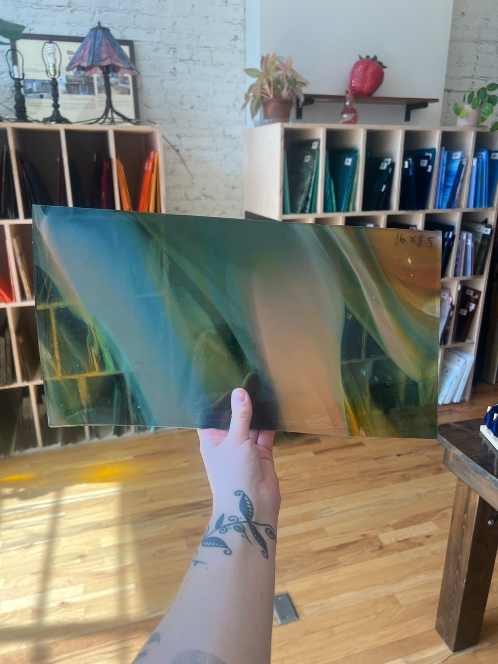 Person holding a large swirled piece of stained glass in a room with bookshelves and decor.