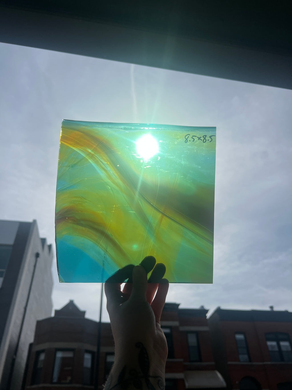 Hand holding a square piece of colorful glass with a blurred cityscape in the background