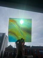 Hand holding a square piece of colorful glass with a blurred cityscape in the background