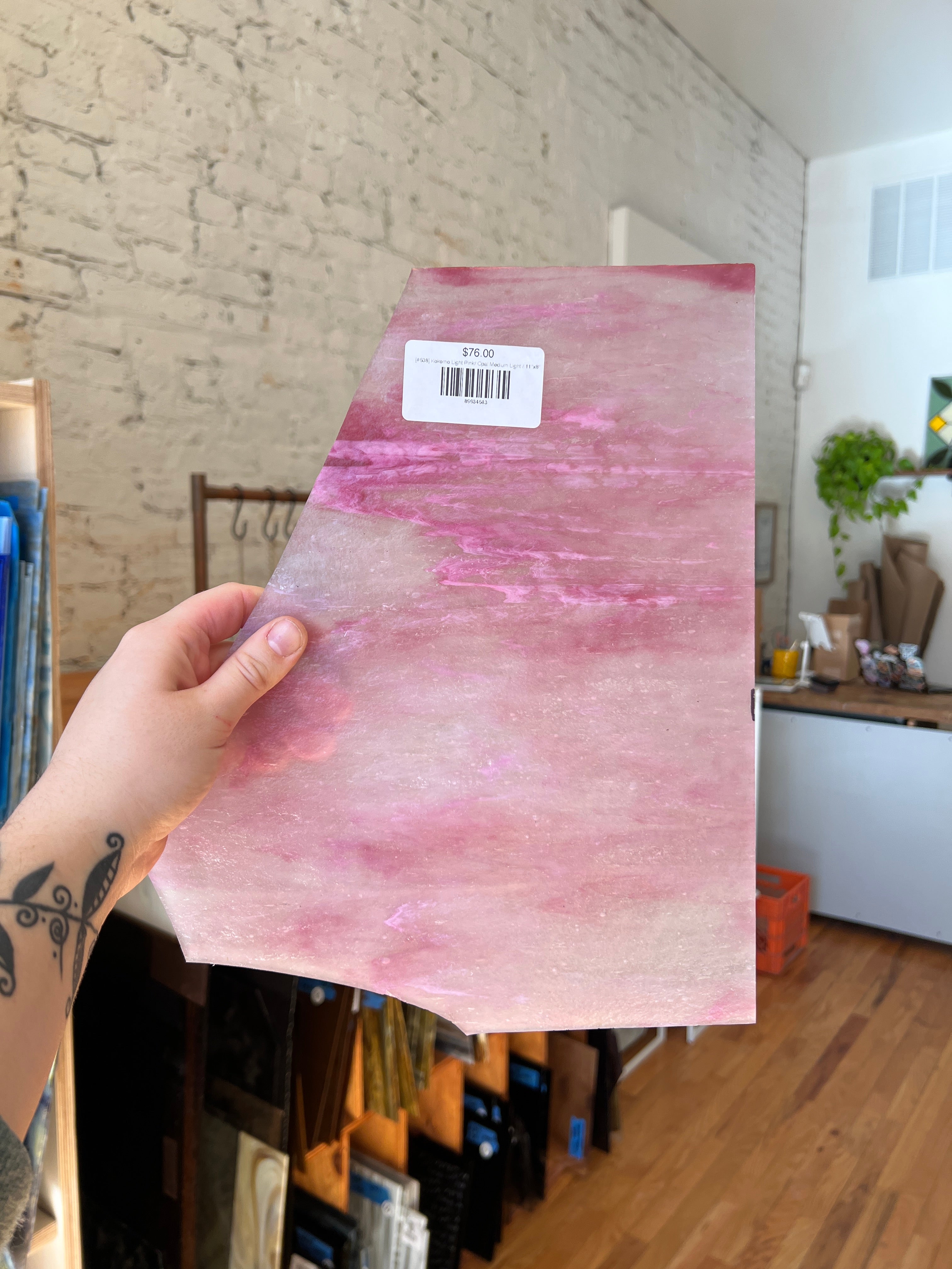 Person holding a pink marbled piece of stained glass with a barcode label indoors.