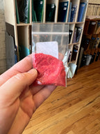 Hand holding a small package of red frit in a store setting