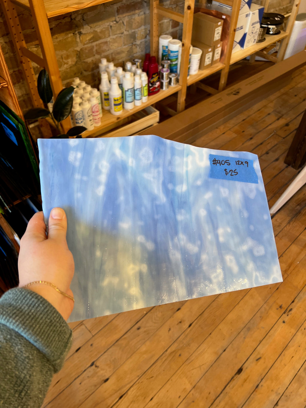 Hand holding a large sheet of glass with a blue and white mottled design, indoors.