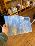 Hand holding a large sheet of glass with a blue and white mottled design, indoors.
