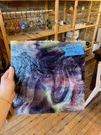 Piece of swirled purple and white stained glass held by a hand with a store setting in the background