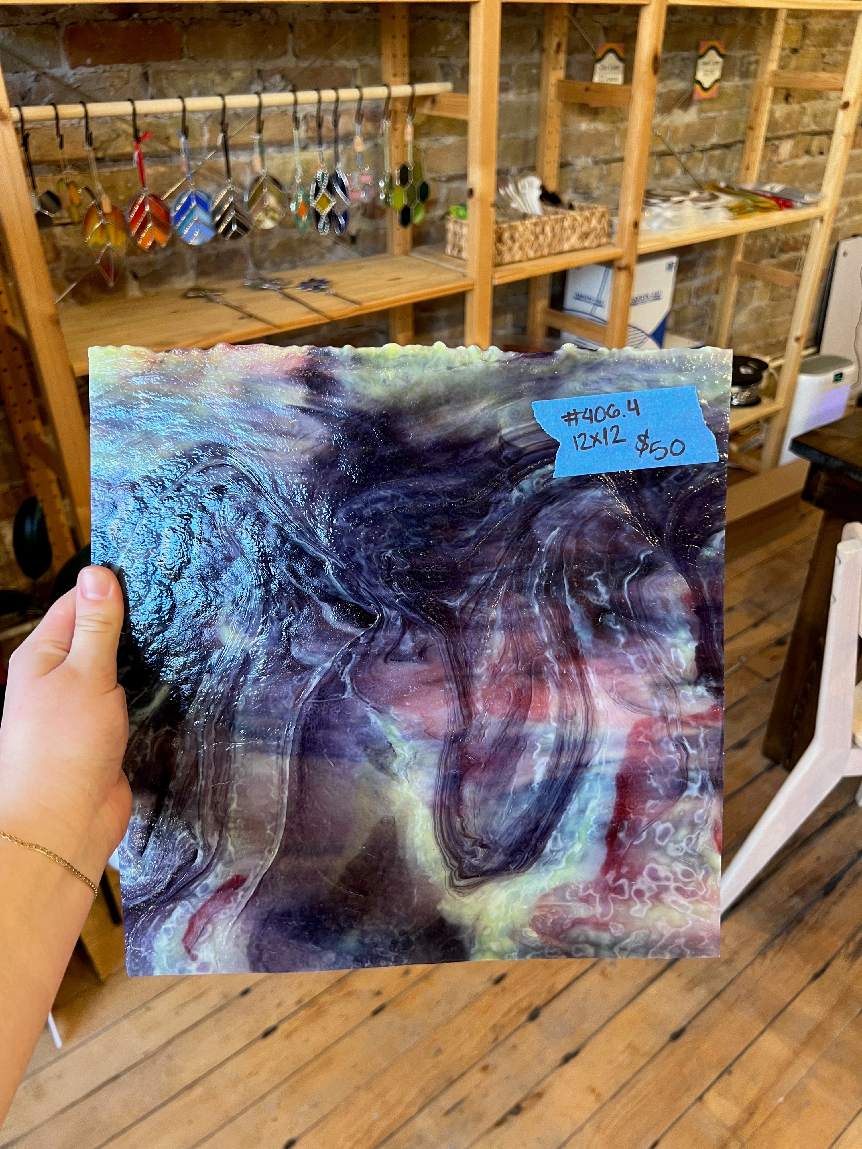 Piece of swirled purple and white stained glass held by a hand with a store setting in the background