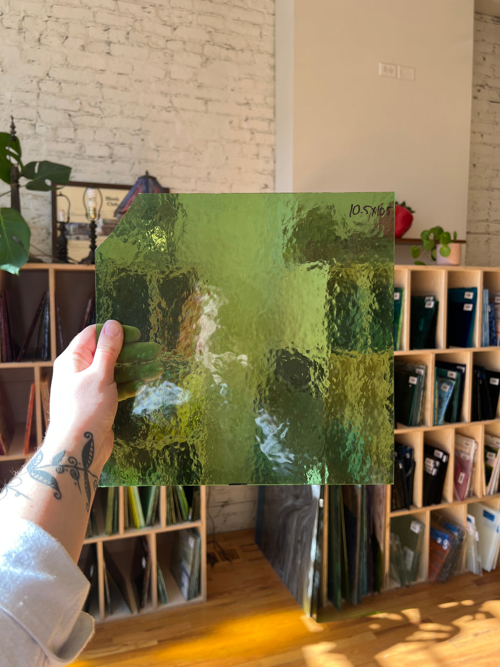 Person holding a green textured piece of stained glass in front of a blurred interior. 