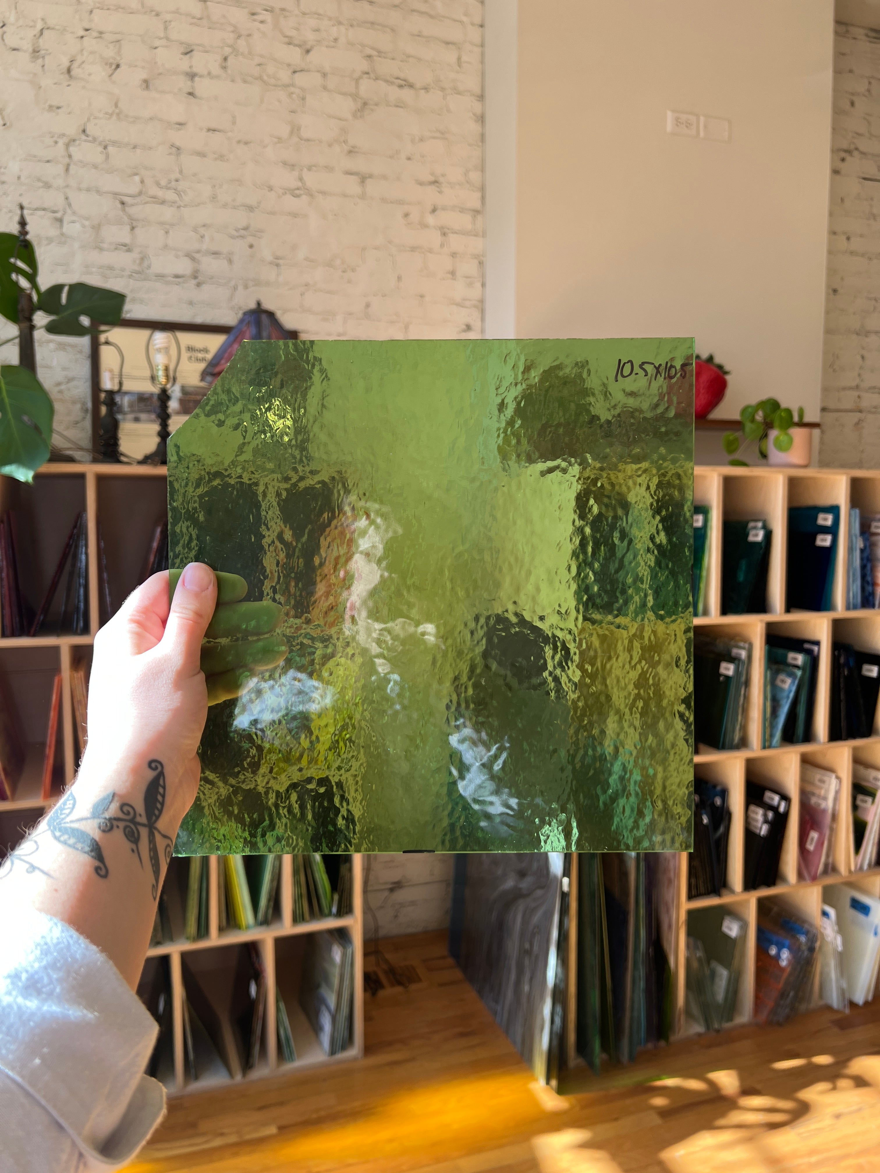 Person holding a green textured piece of stained glass in front of a blurred interior. 