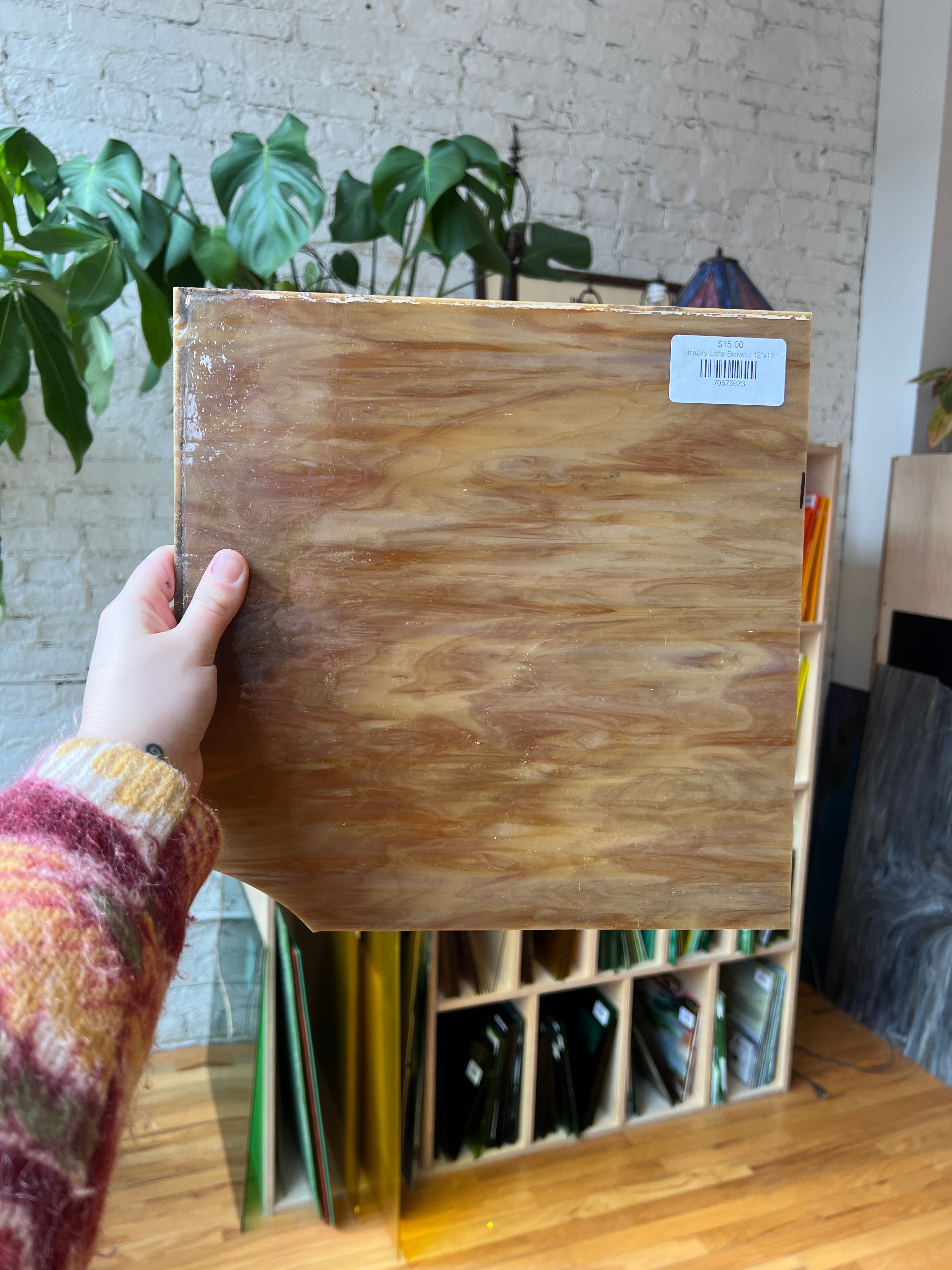 Person holding a piece of brown swirled stained glass with a plant in the background