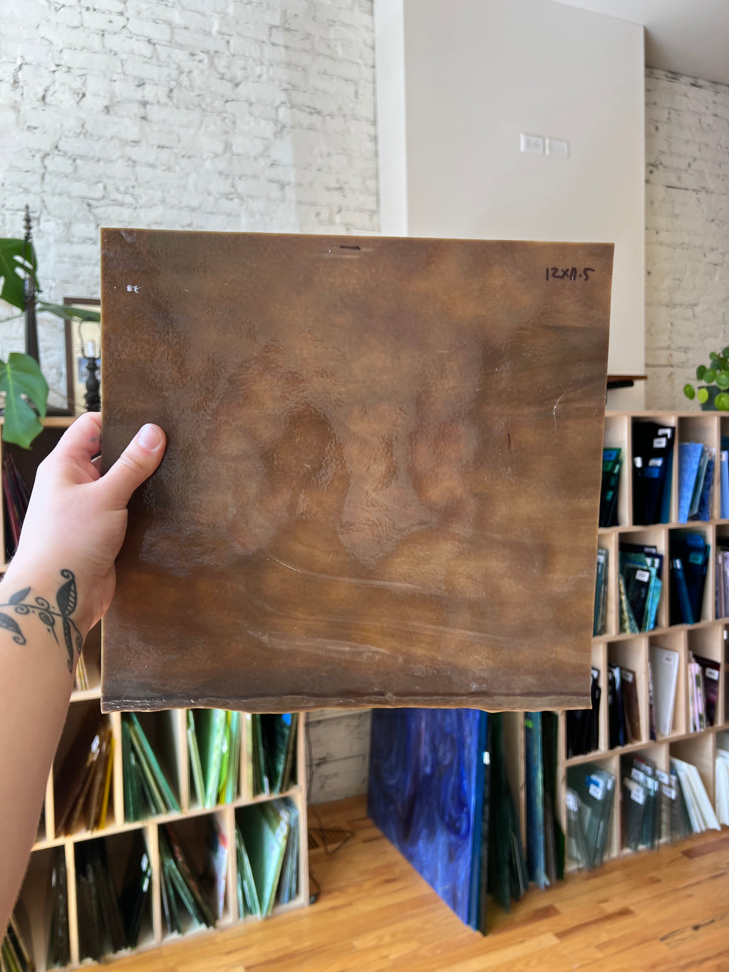 Brown piece of glass held by a hand in a room with a white wall and wooden floor.
