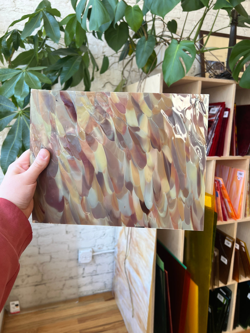 Person holding a colorful abstract piece of stained glass in front of a bookshelf.