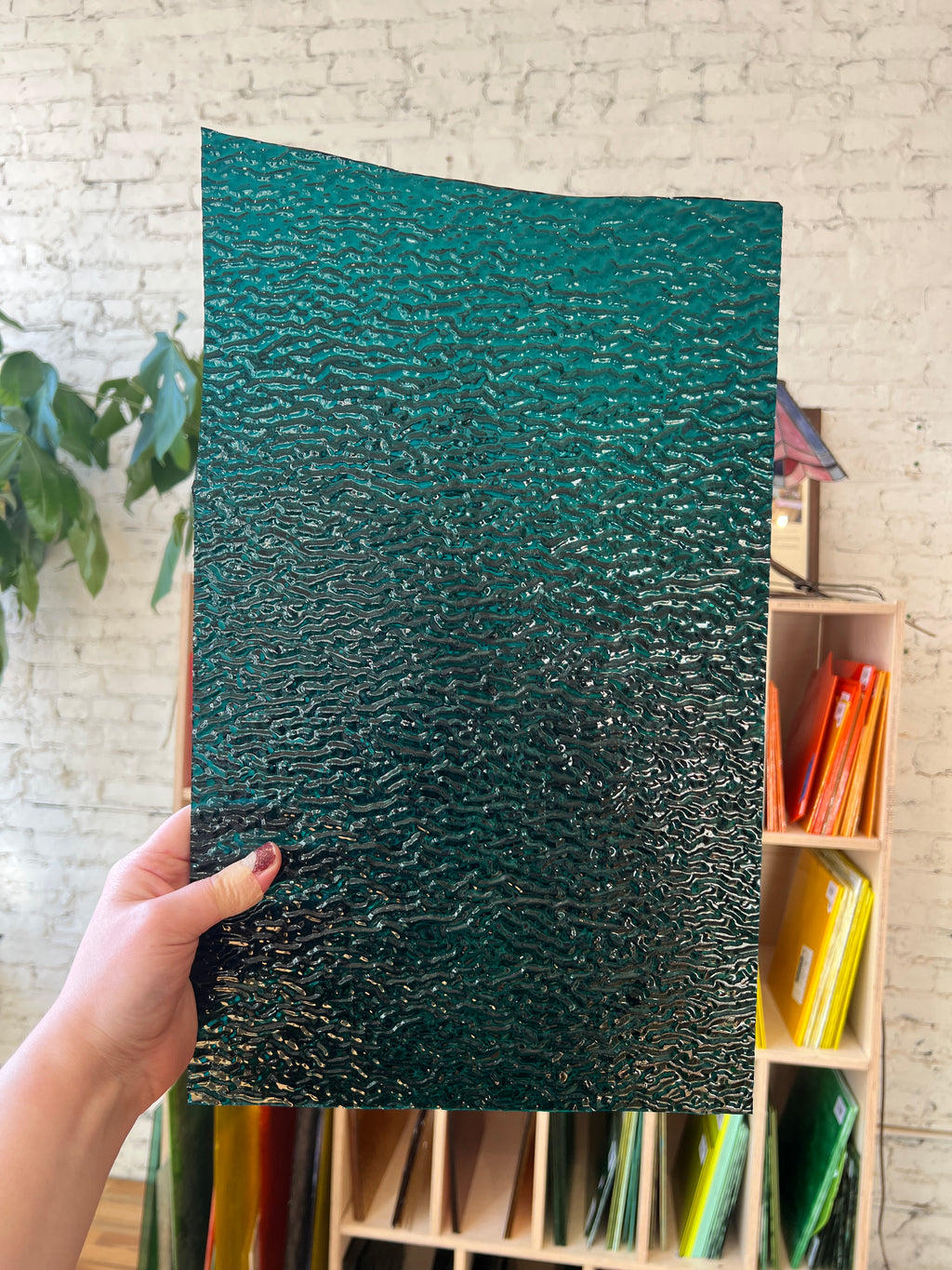 Hand holding a textured green piece of stained glass in front of a shelf