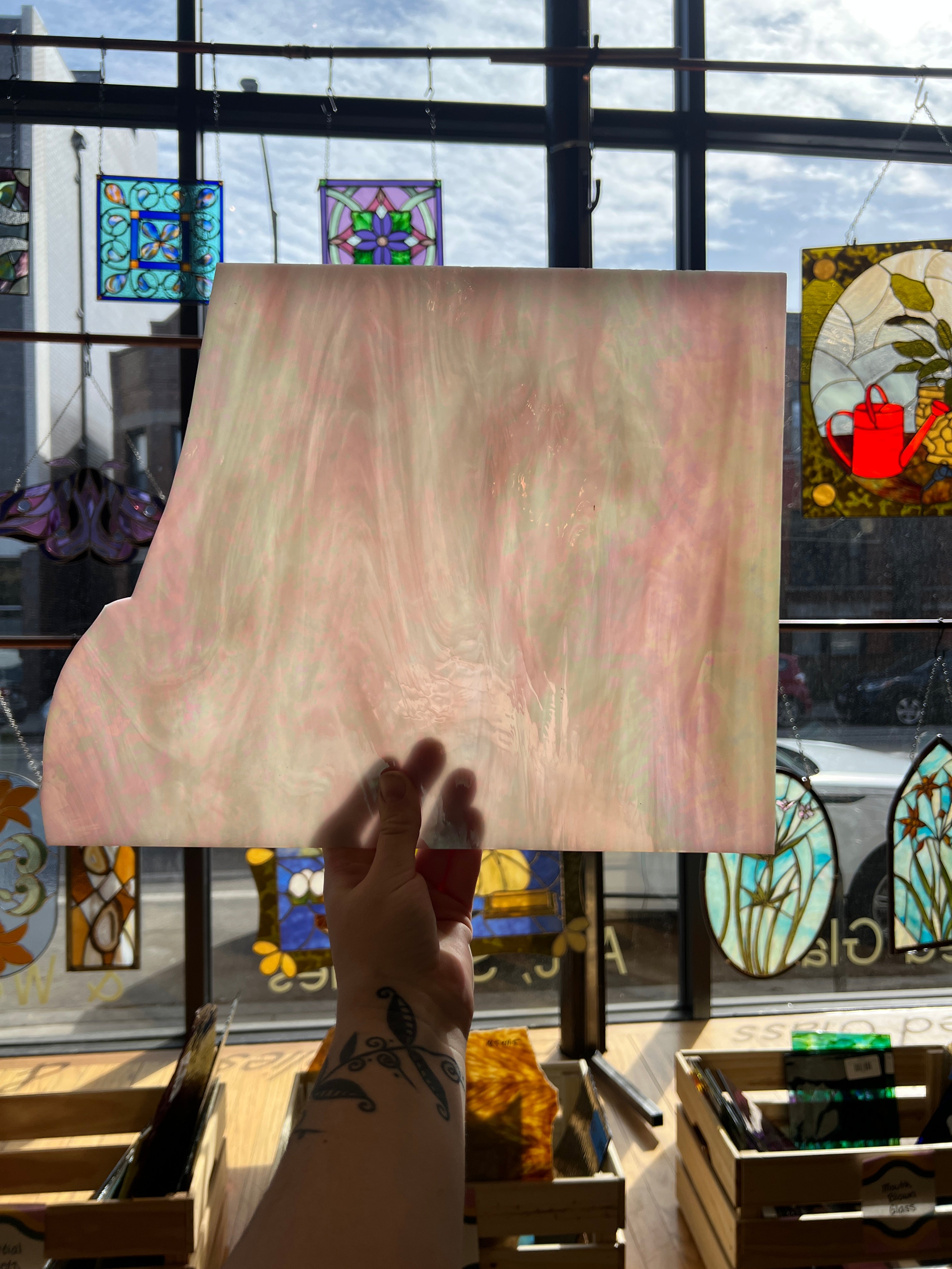 Person holding a pale pink piece of stained glass in front of a stained glass window