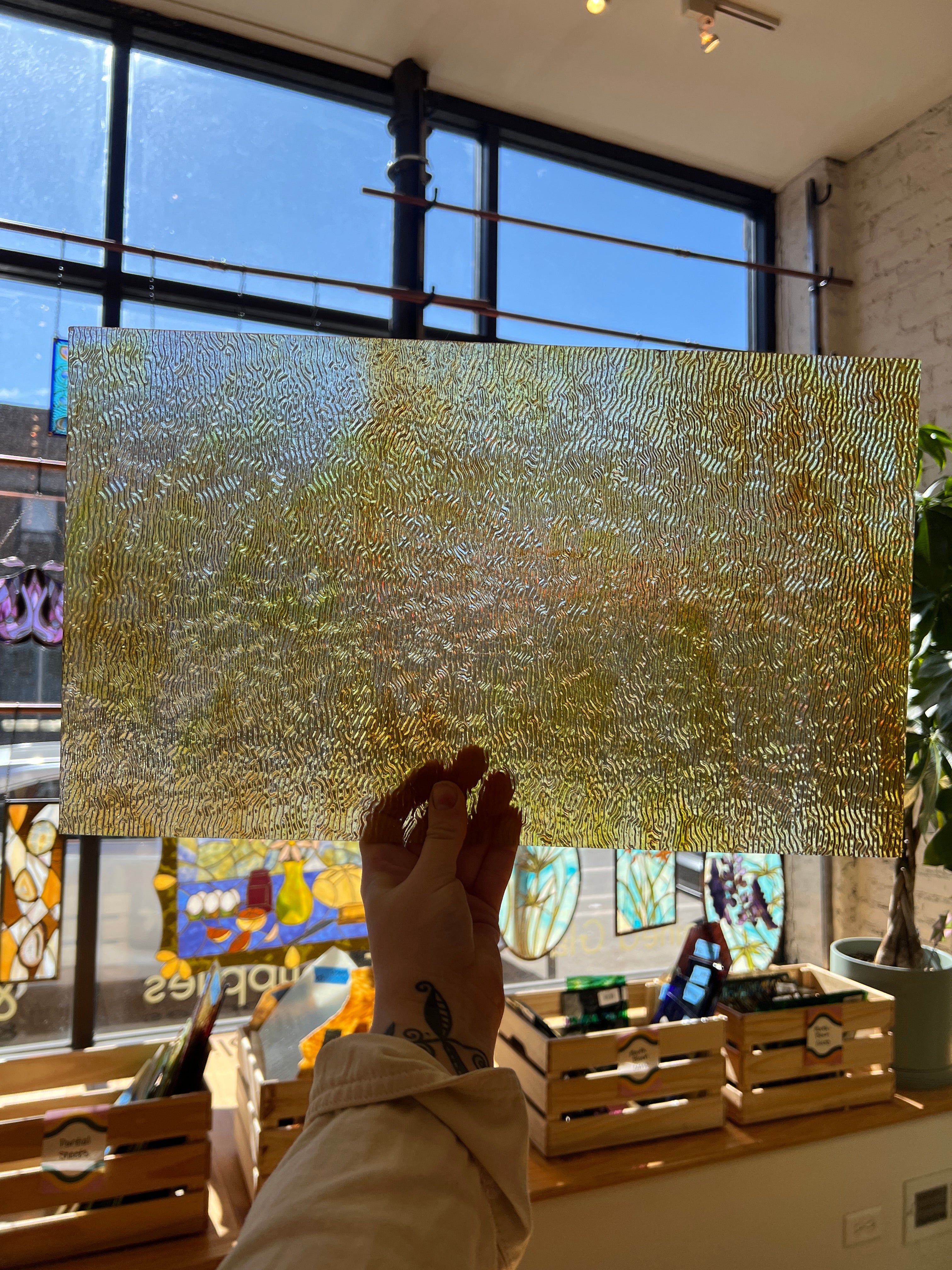 Hand holding a textured gold sheet of glass with stained glass windows in the background