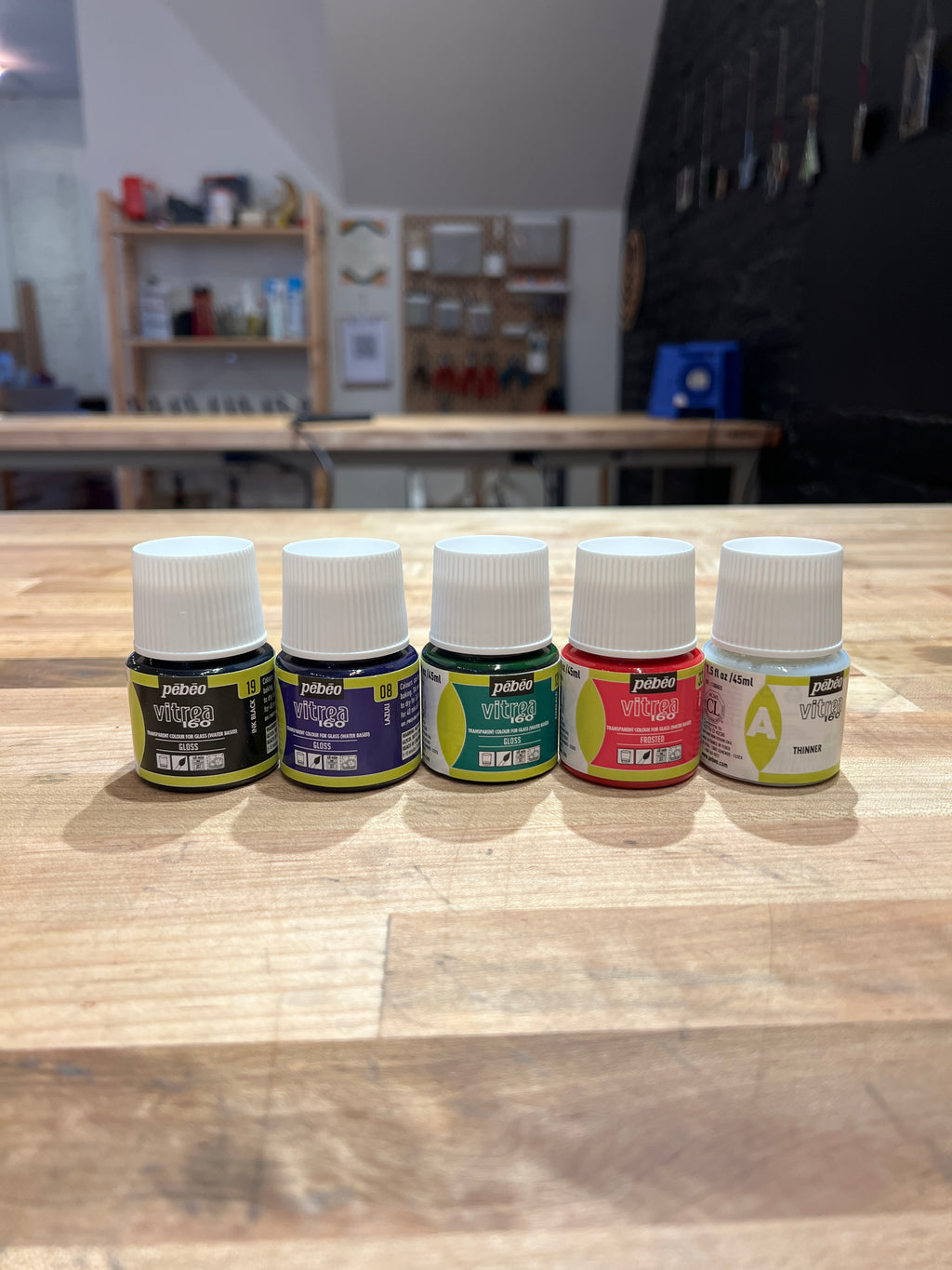 Set of small stained glass supply bottles on a wooden surface with a blurred indoor background