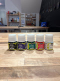 Set of small stained glass supply bottles on a wooden surface with a blurred indoor background