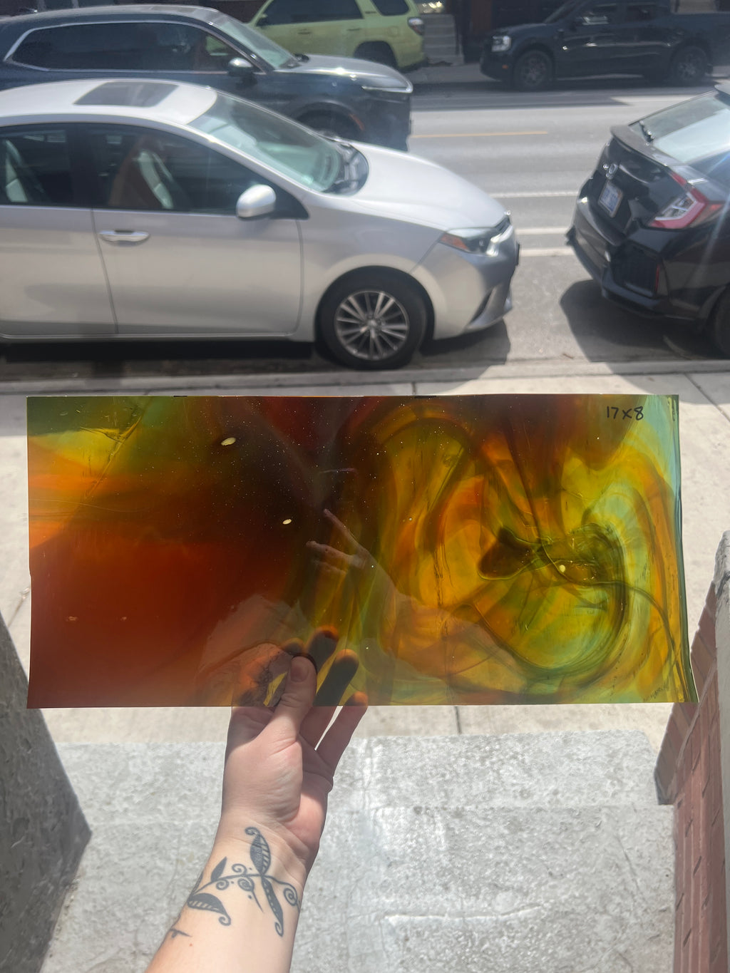 Swirled piece of stained glass held by a hand on a city street with cars in the background