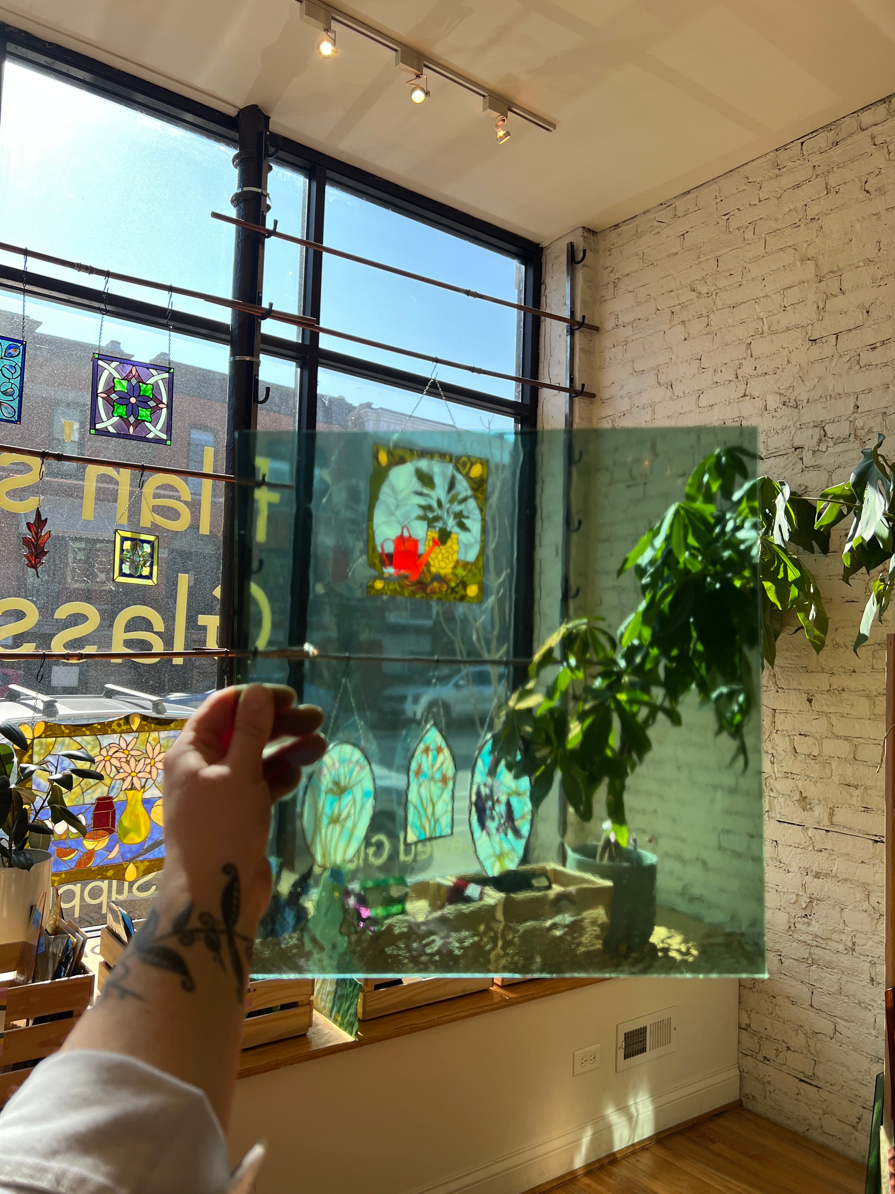 Person holding a green transparent piece of stained glass in front of a blurred sunny window. 