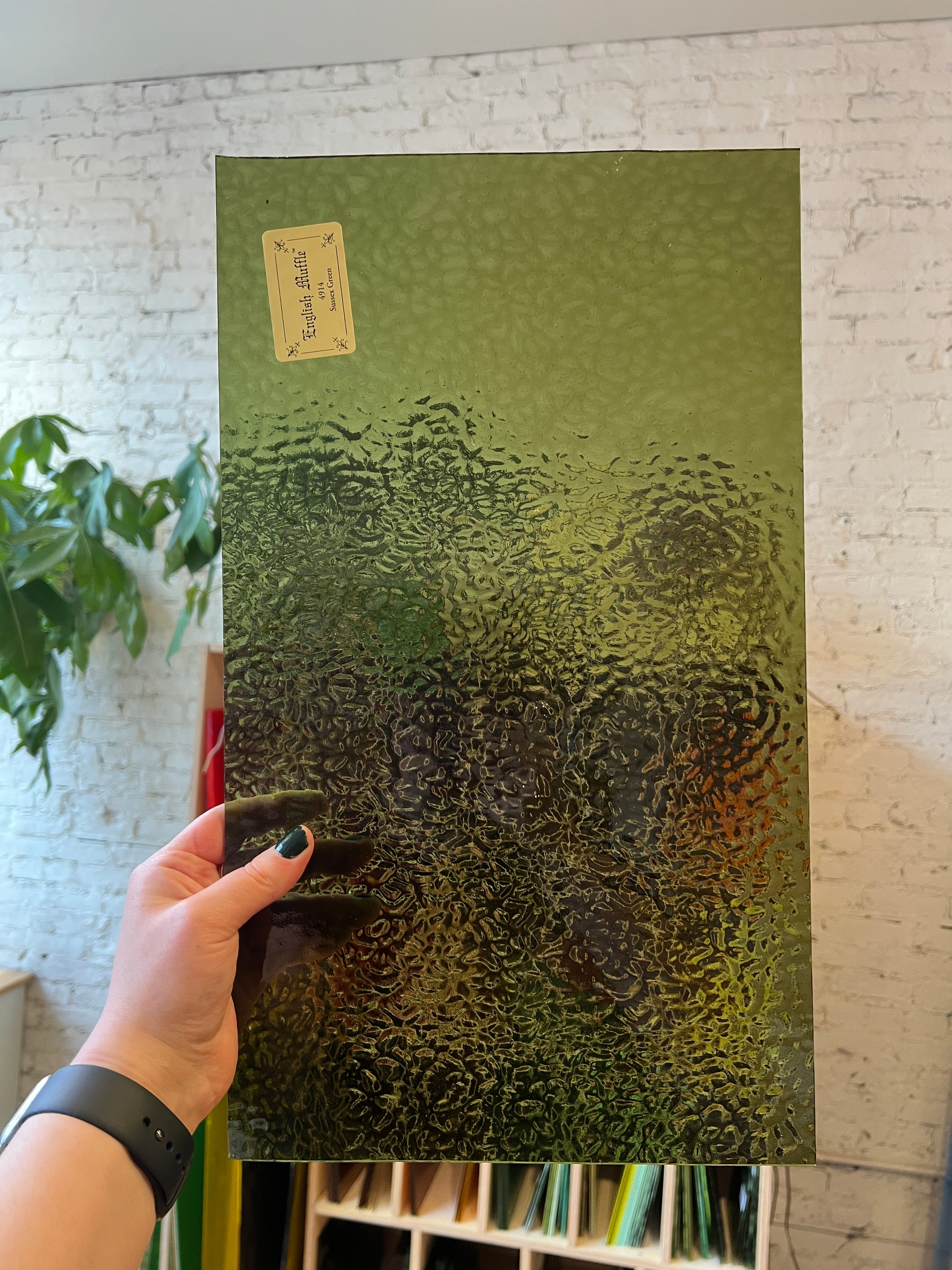 Person holding a green textured piece of stained glass with a blurred background