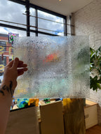 Decorative floral textured glass panel with a hand touching it, indoors with a window view.