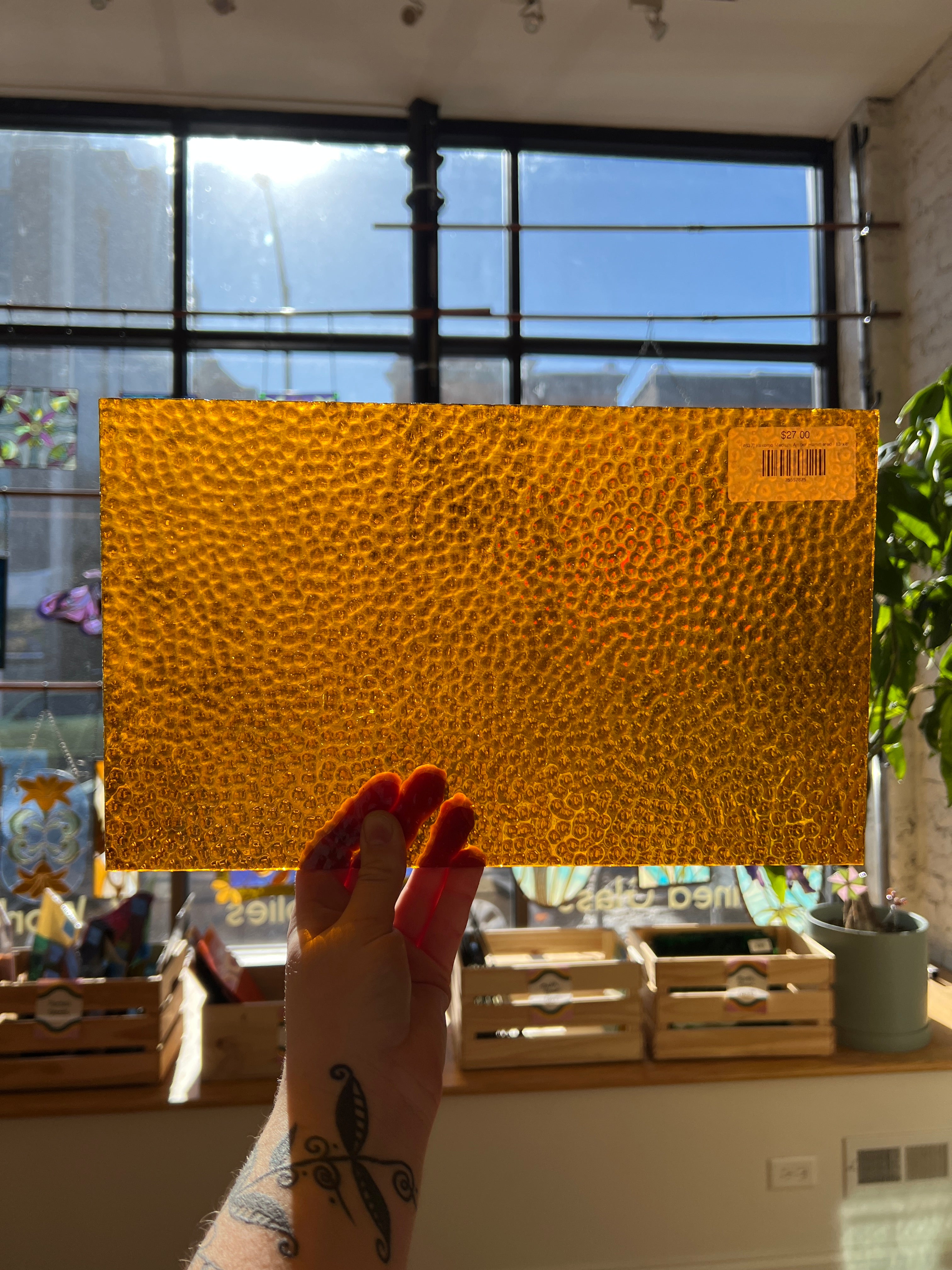 Hand holding a textured yellow piece of stained glass with a blurred indoor background