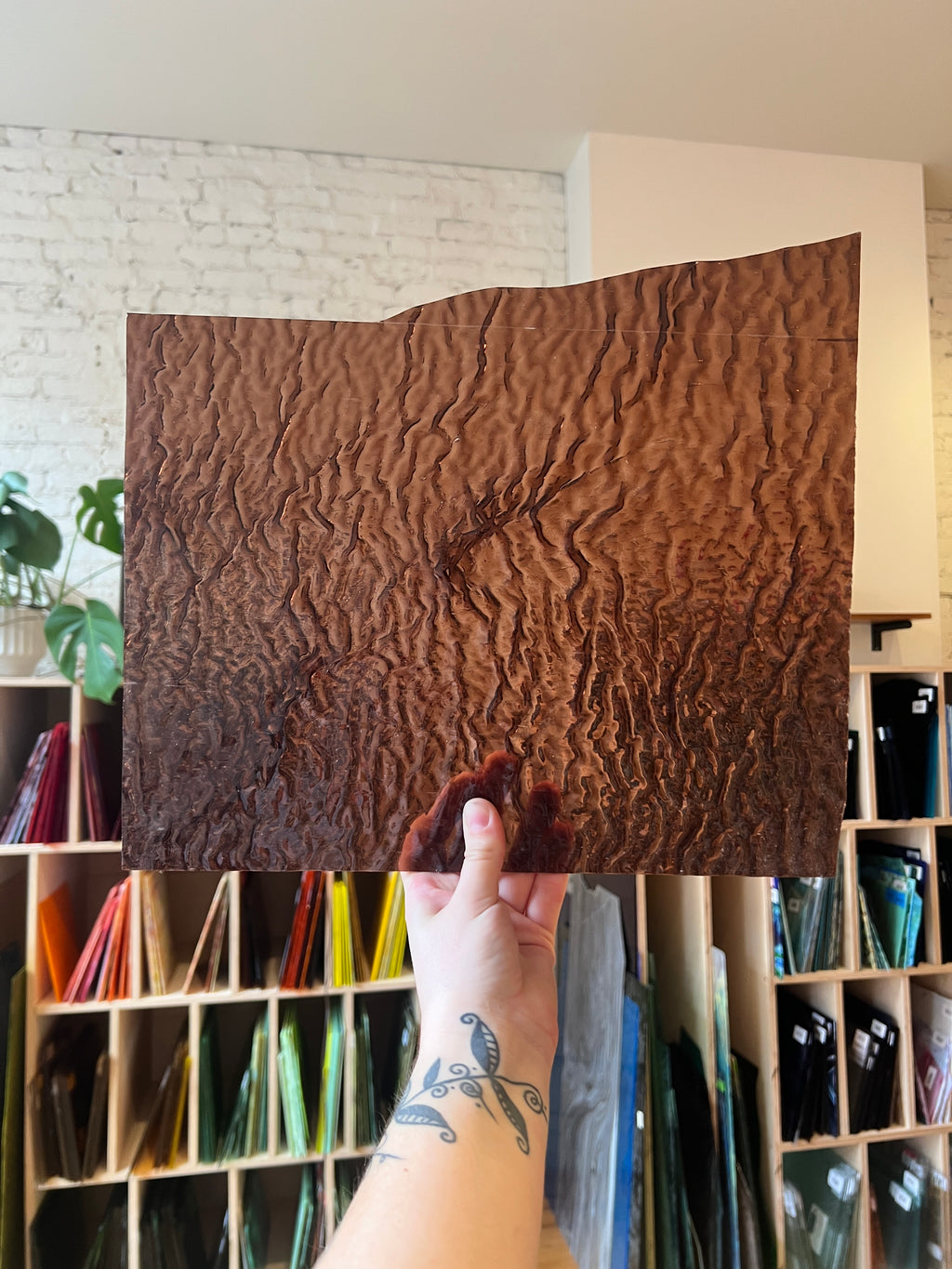 Brown textured piece of stained glass held by a hand in front of a bookshelf.