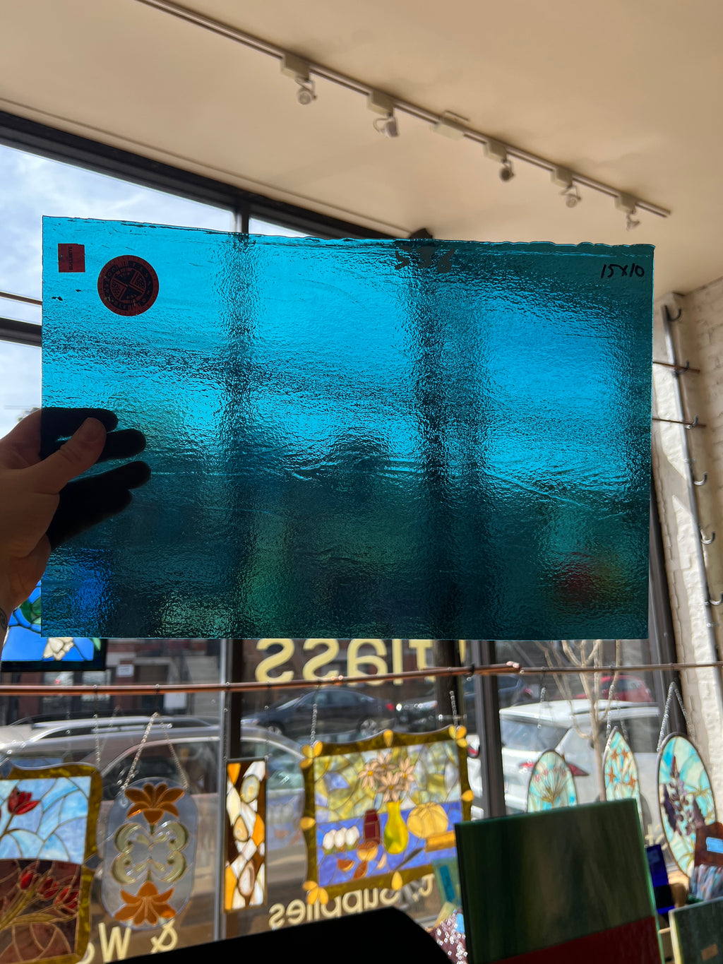 Blue textured piece of glass held by a hand with a stained glass window in the background