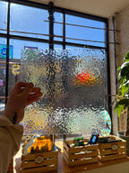 Hand touching a textured glass piece with a blurred outdoor view