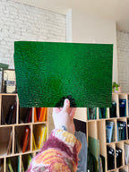 Green textured sheet of glass held by a person with a blurred background