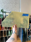 Person holding a neutral colored piece of mottled stained glass in an indoor setting. 