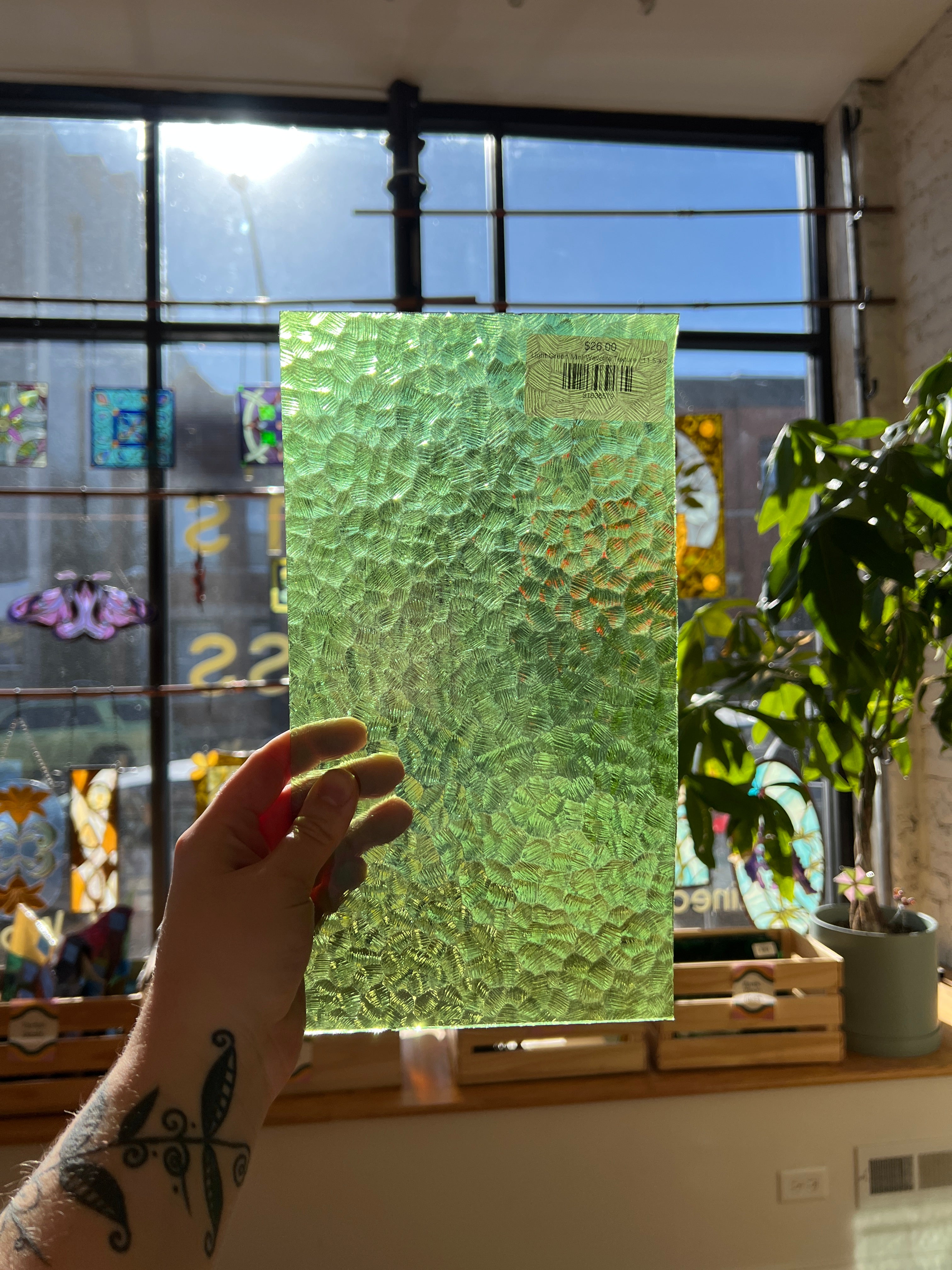 Hand holding a green textured piece of stained glass in front of a window with stained glass