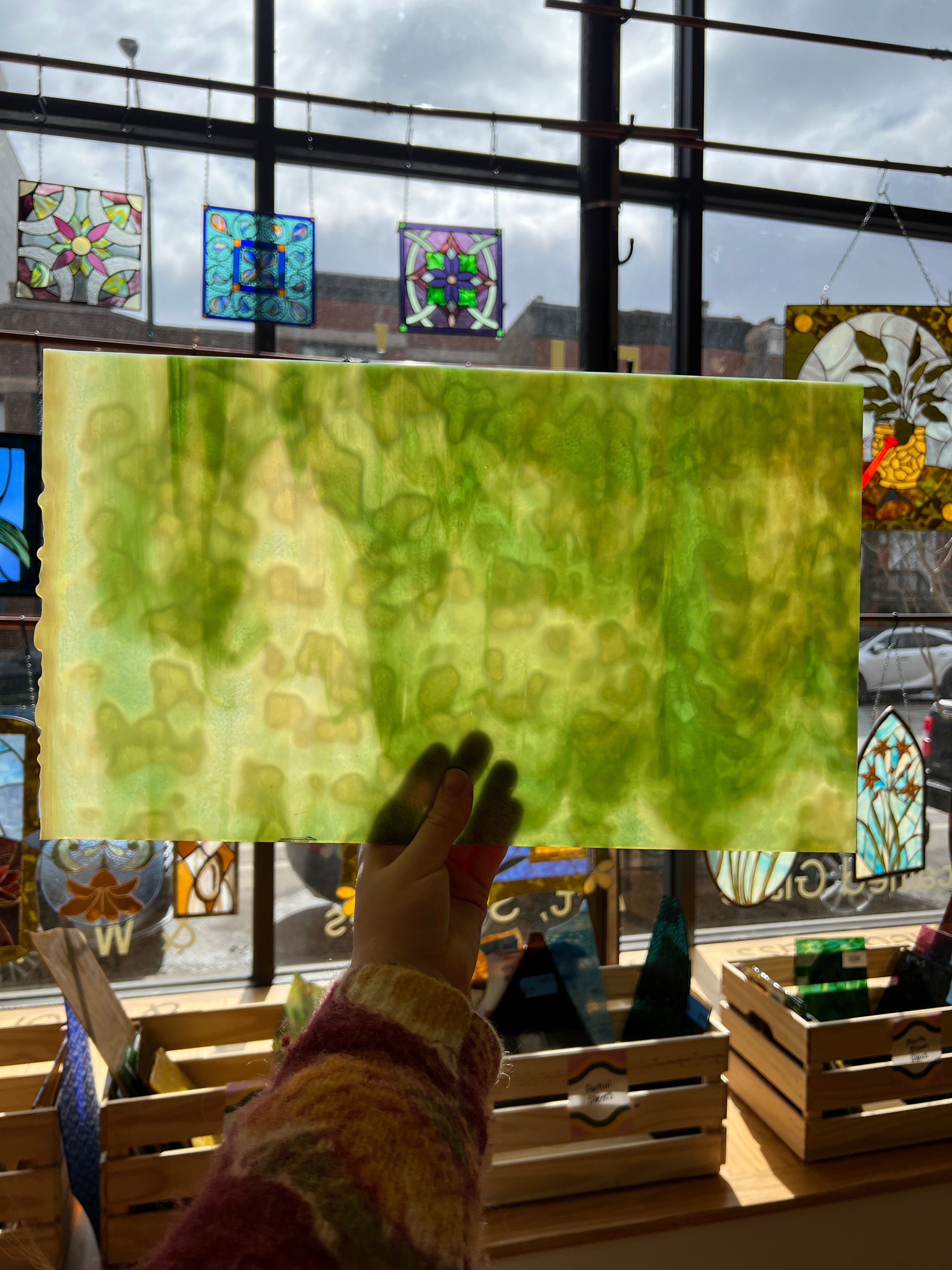 Green textured piece of glass with a hand holding it, surrounded by colorful stained glass windows.