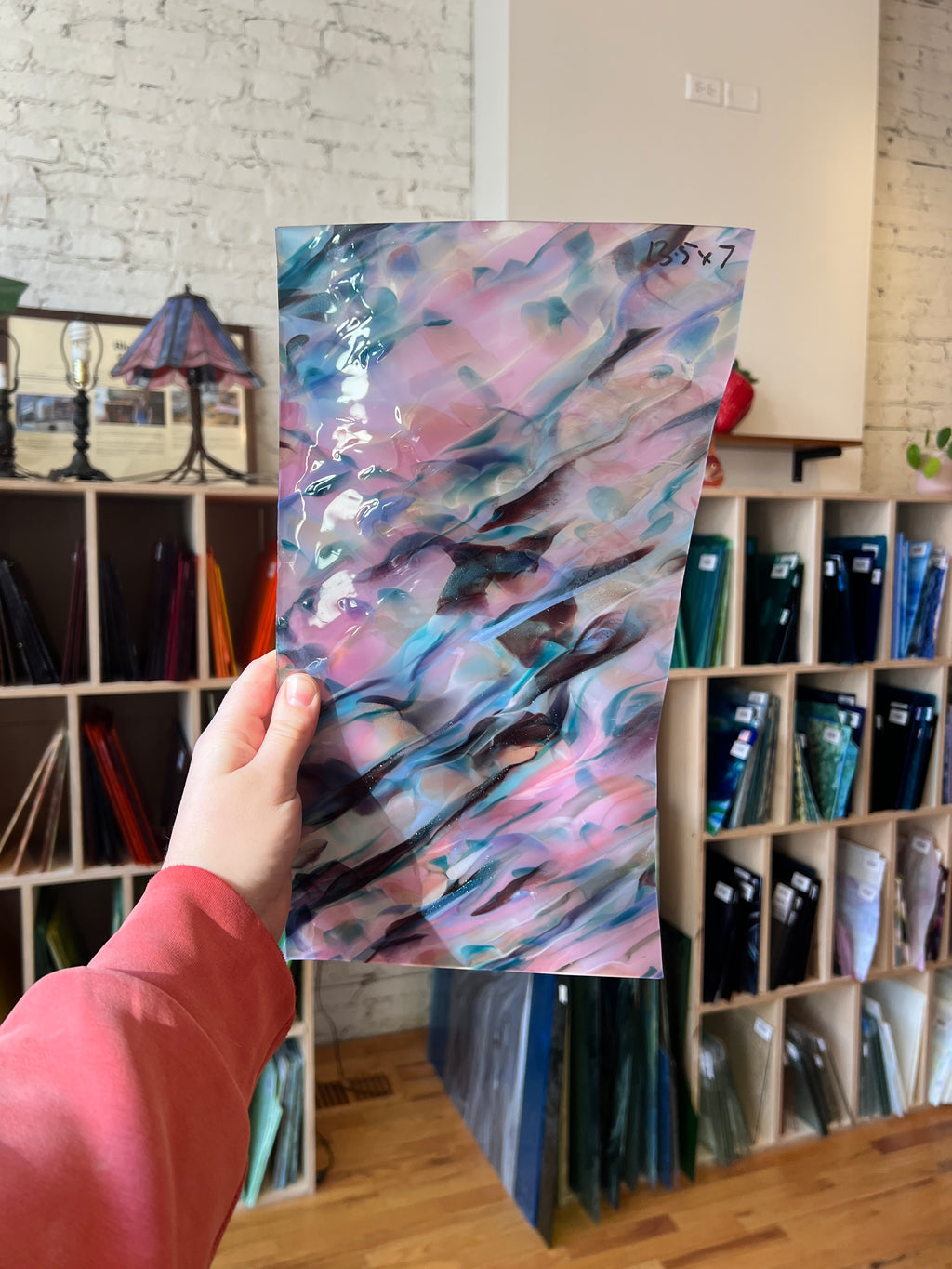 Hand holding a colorful abstract piece of stained glass in front of a bookshelf.