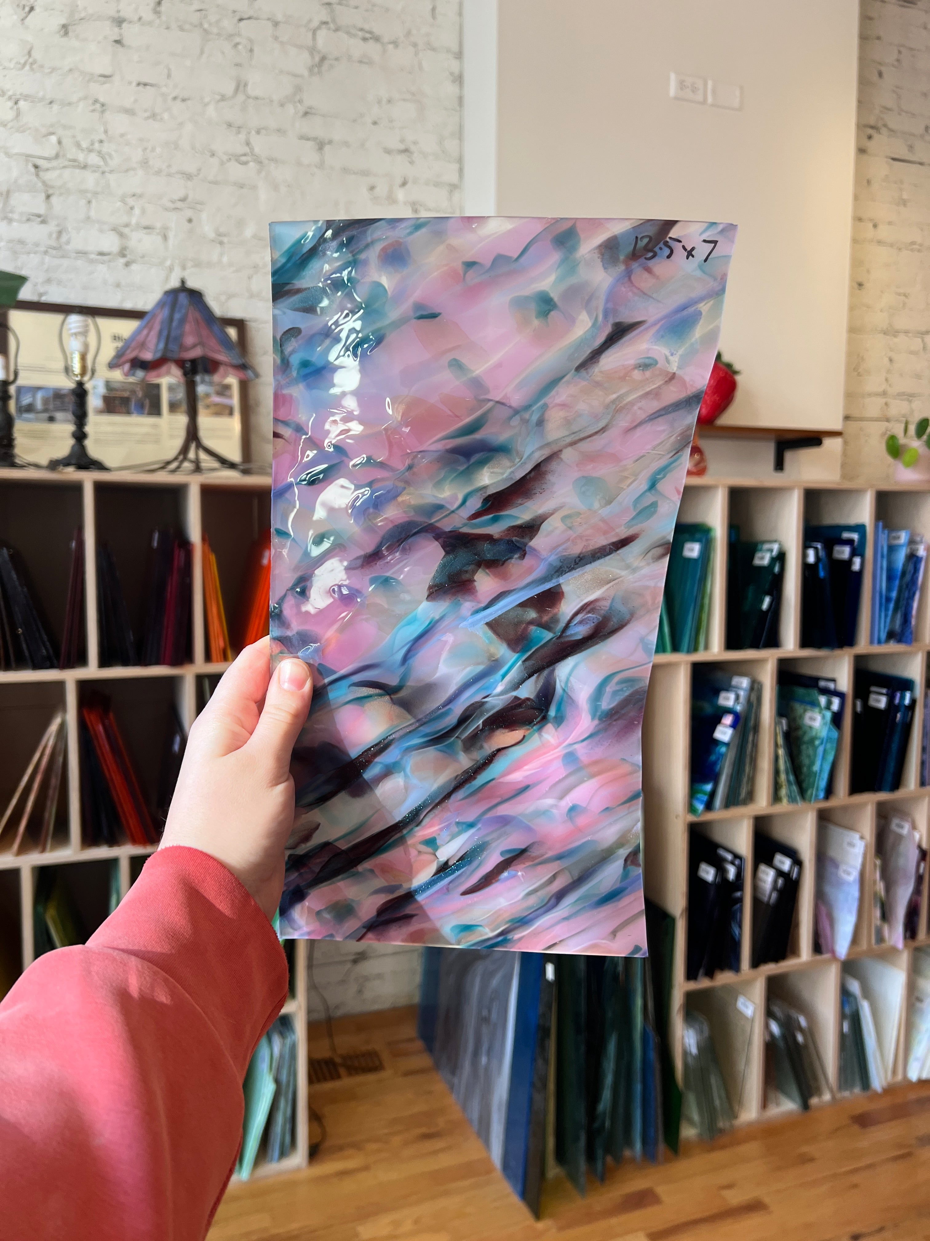 Hand holding a colorful abstract piece of stained glass in front of a bookshelf.
