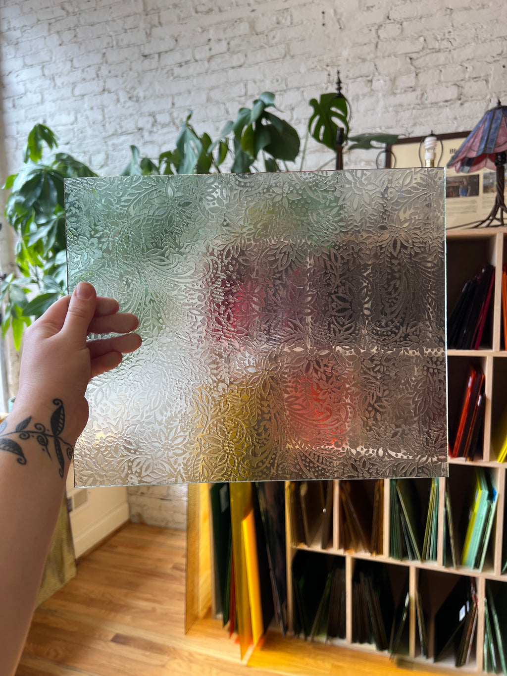 Decorative floral textured glass panel held by a hand with a blurred indoor background