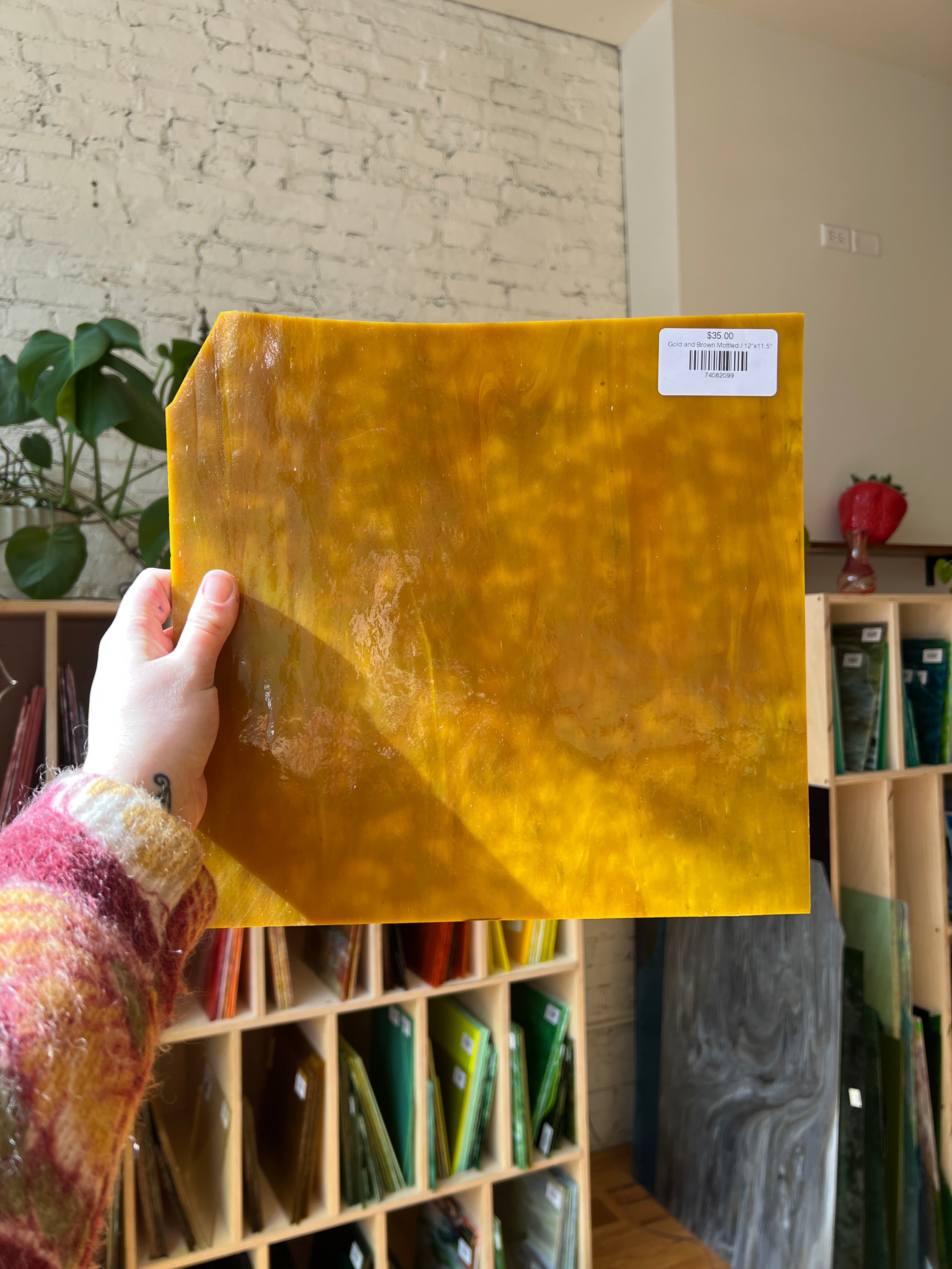 Yellow piece of stained glass with a hand holding it, before a surface with various items in the background.