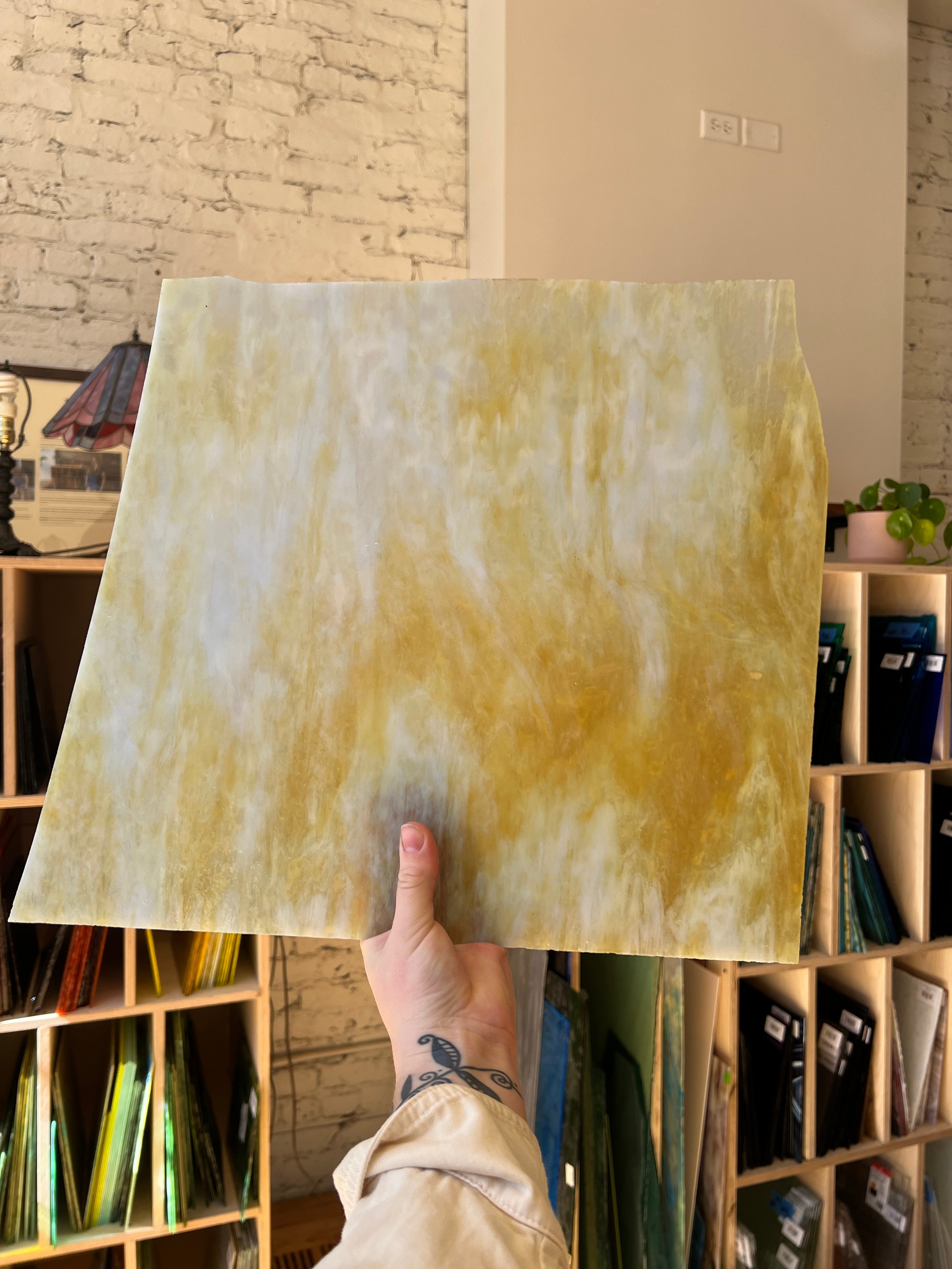 Person holding a large rectangular piece of yellowish glass against a wall with shelves.
