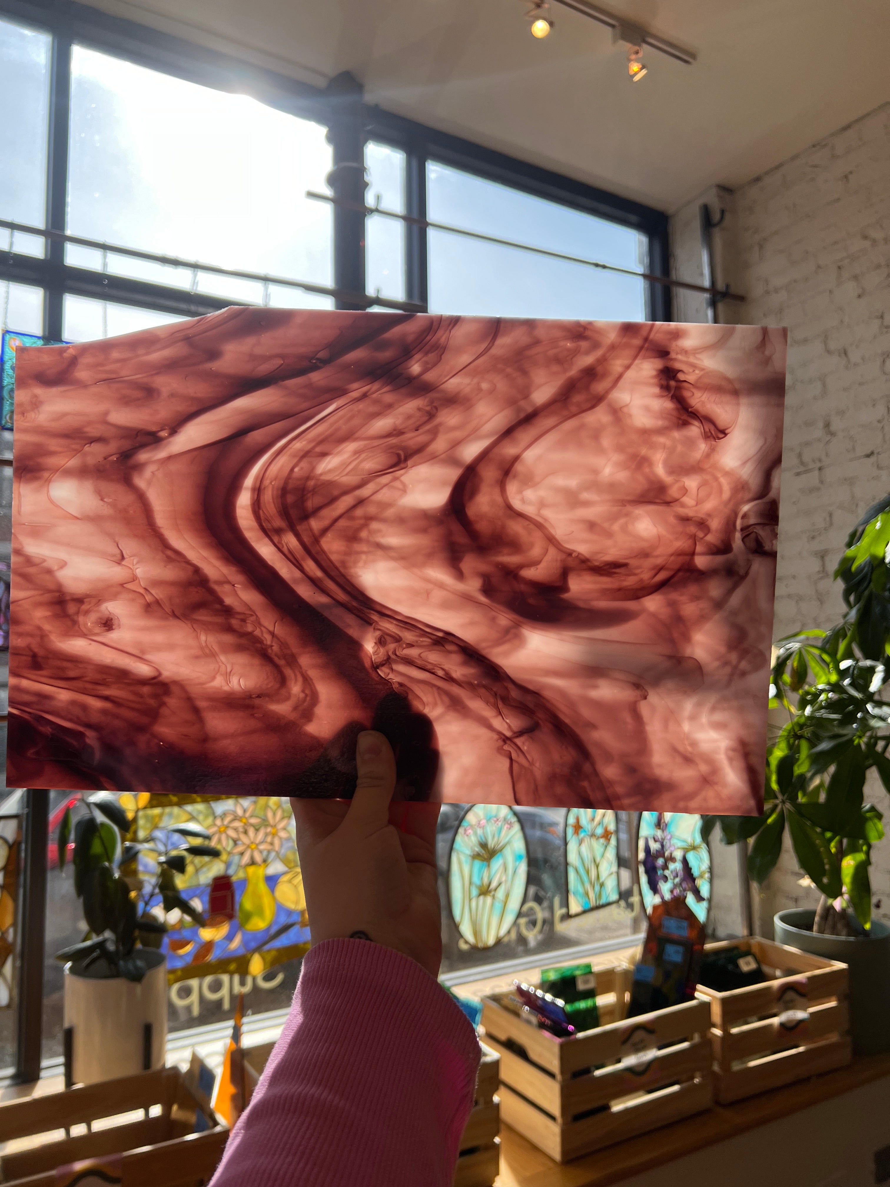 Person holding a large piece of stained glass with a swirling purple and white pattern in an indoor setting.