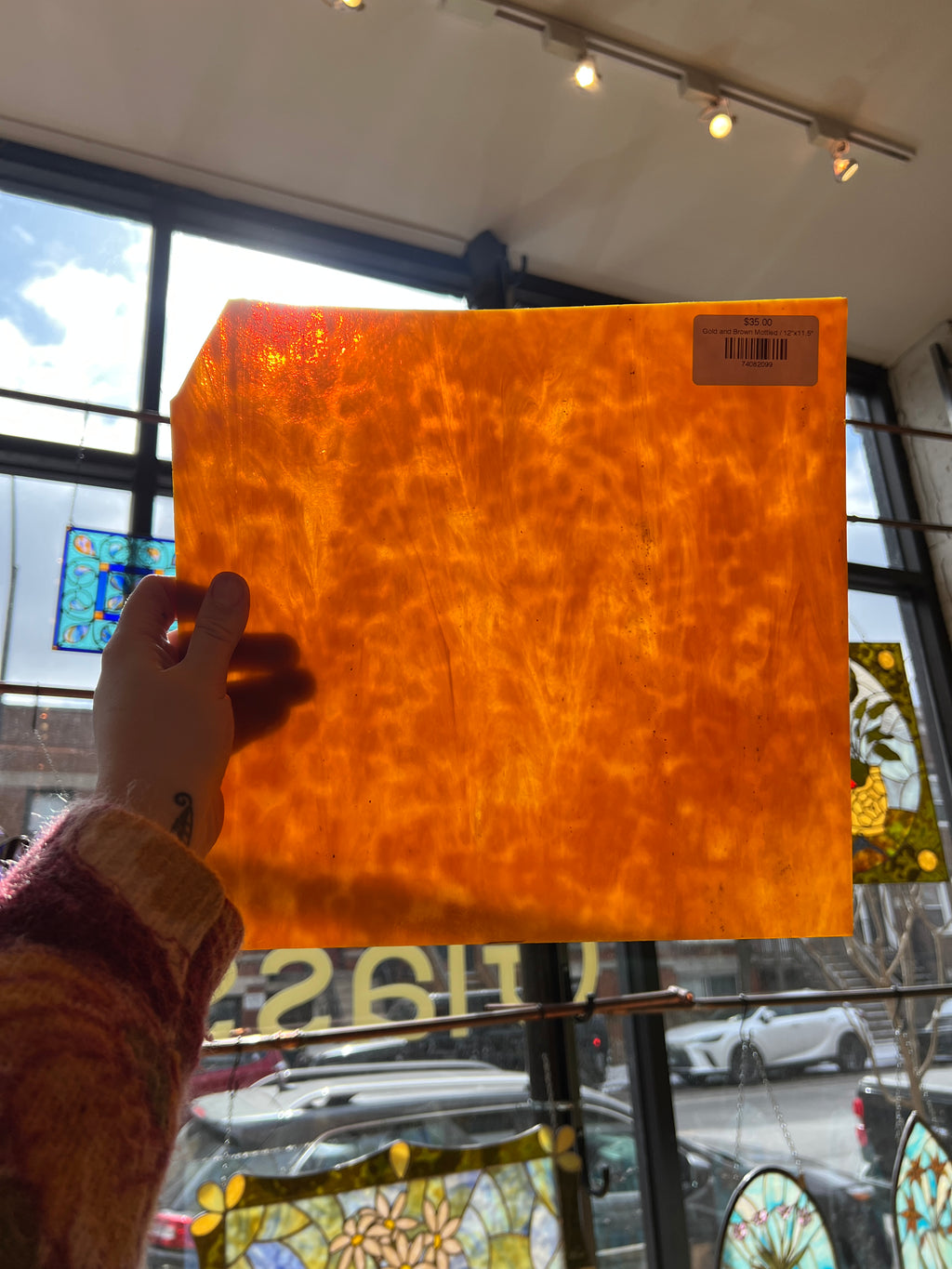 Large orange piece of stained glass held by a person in front of a store window with stained glass.