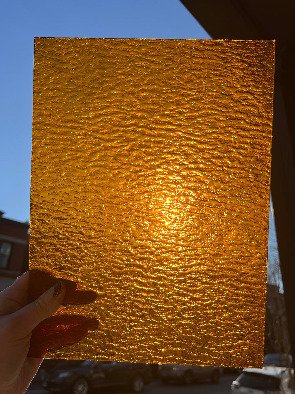 Gold textured stained glass held by a hand against a blue sky