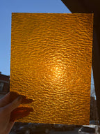 Gold textured stained glass held by a hand against a blue sky