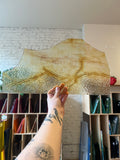Person holding a neutral colored textured sheet of stained glass in an indoor setting. 