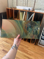 Person holding a rectangular piece of stained glass with abstract design in a room with shelves and records.