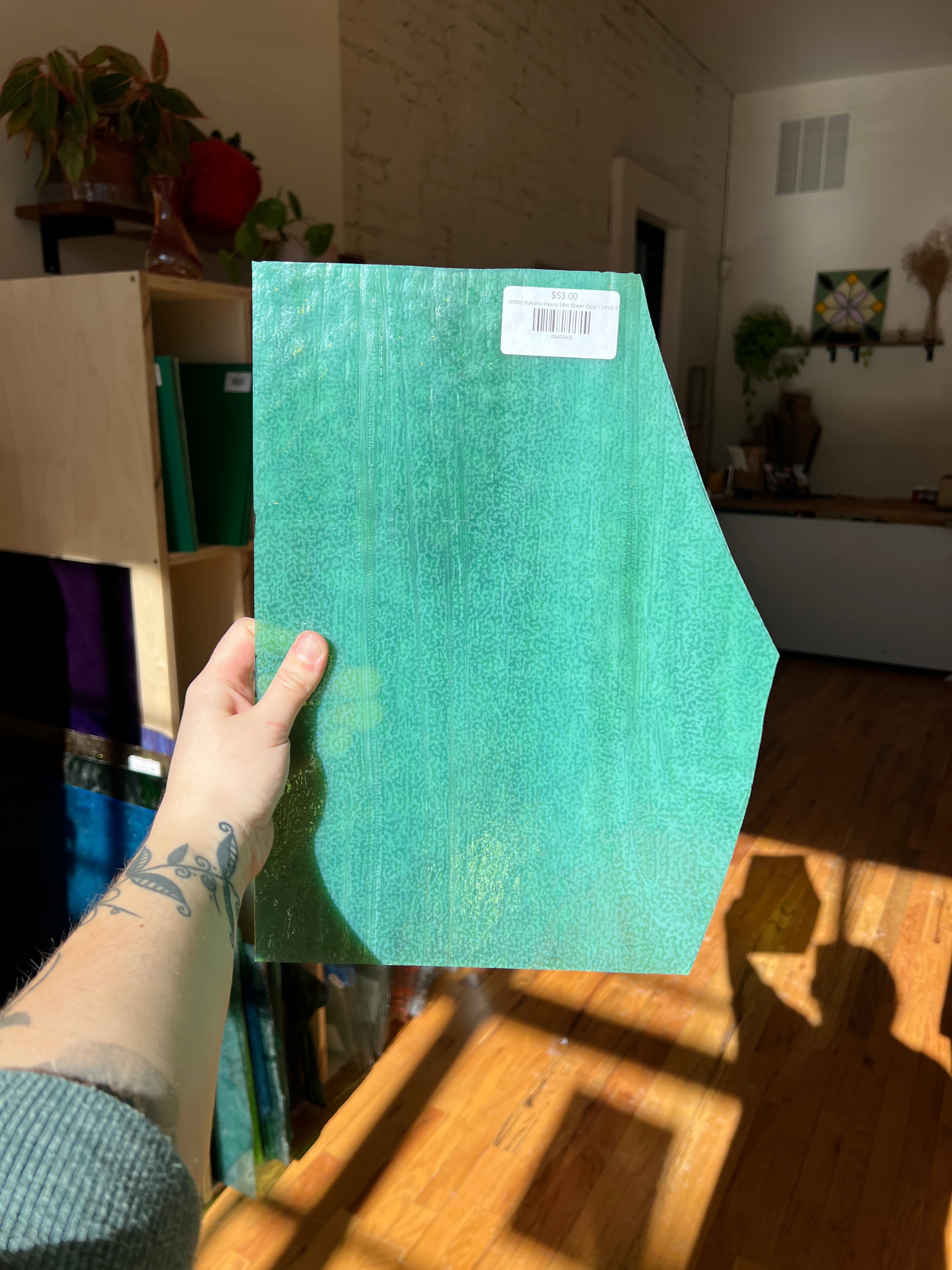 Person holding a green textured piece of stained glass with a label in an indoor setting
