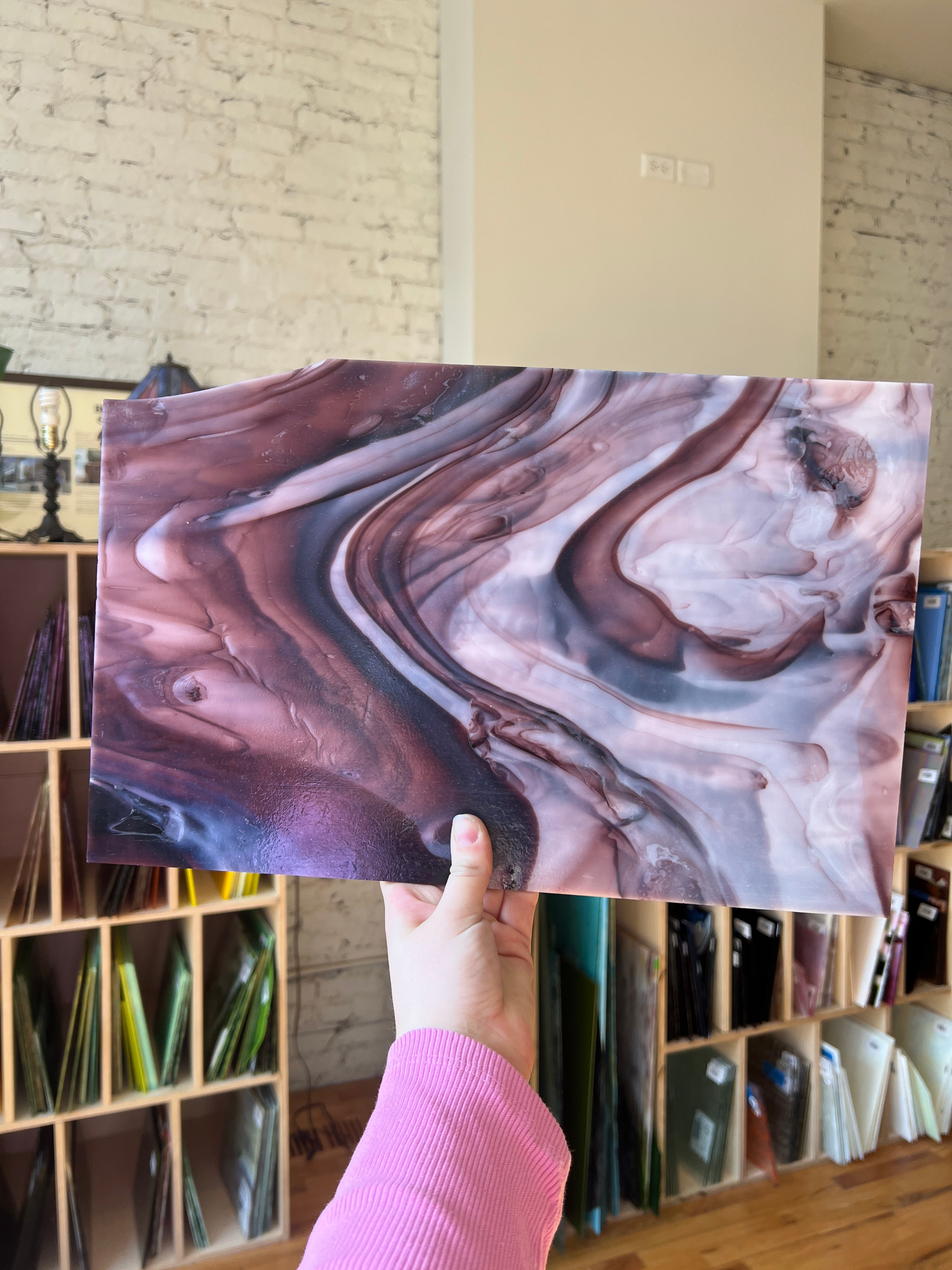 Person holding a piece of stained glass with dark purple and white swirls.