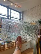 Person holding a textured glass panel indoors with a light background