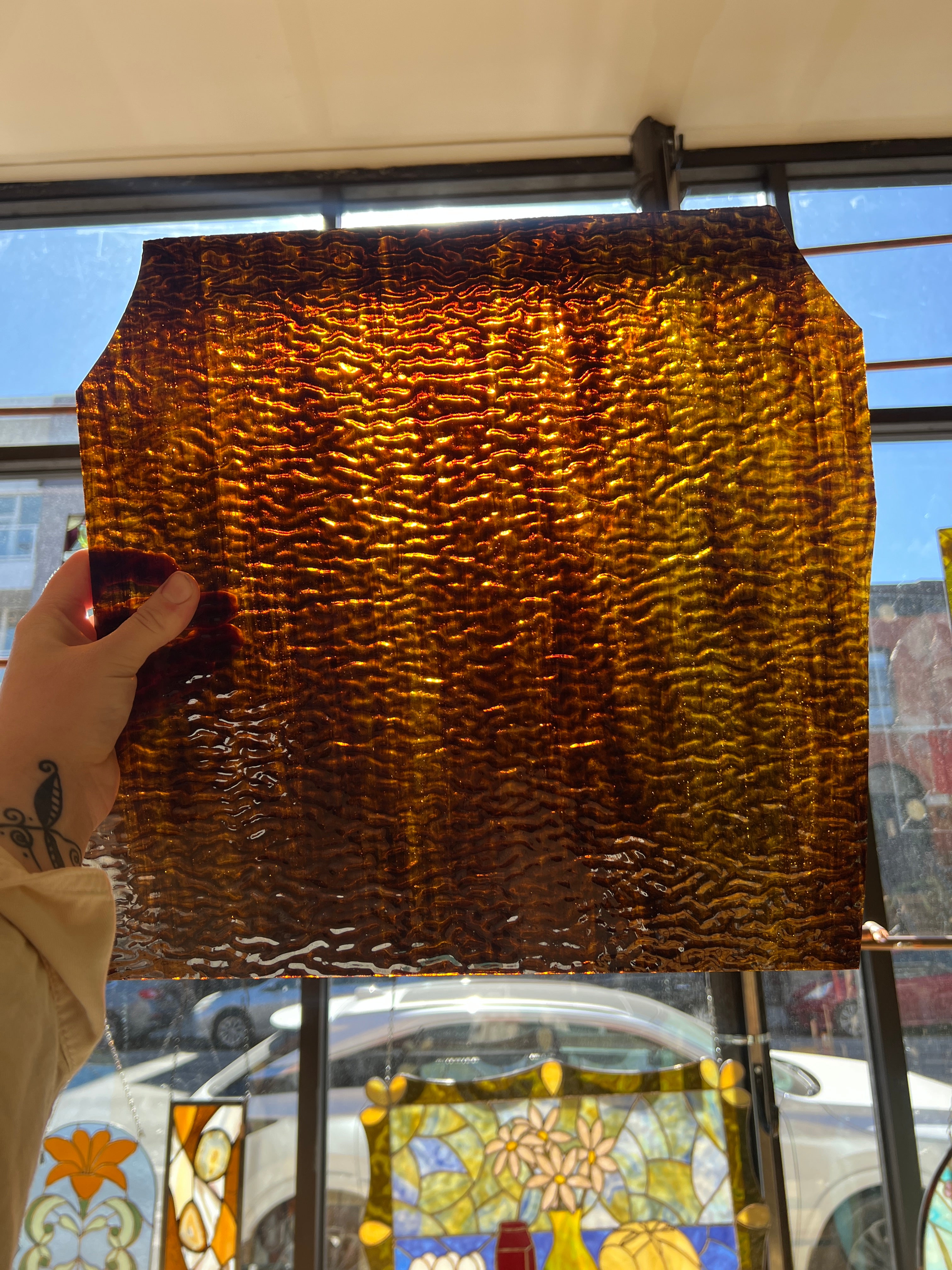 Textured brown piece of stained glass held by a hand in front of a stained glass window