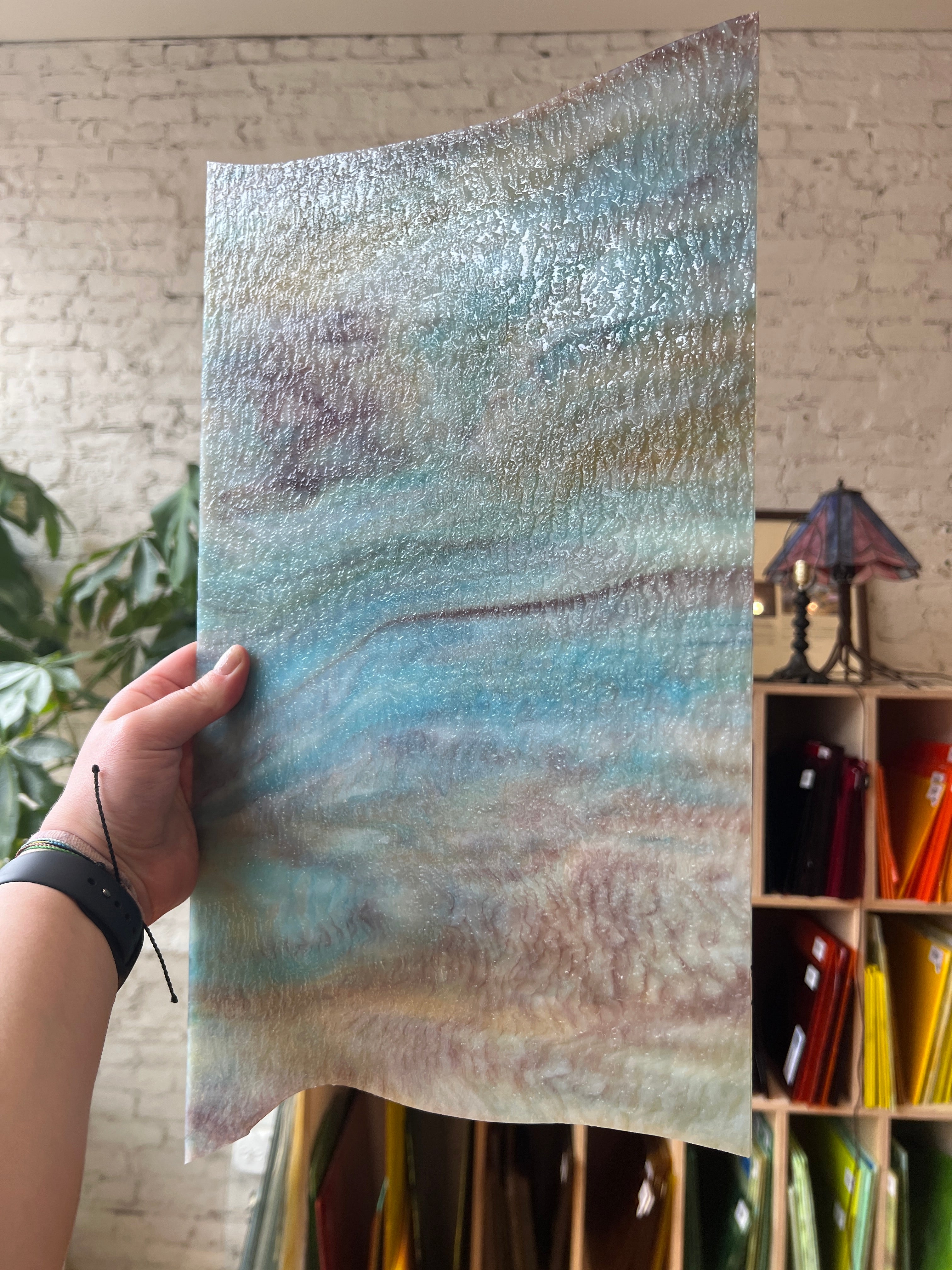 Hand holding a piece of textured stained glass with a blurred background