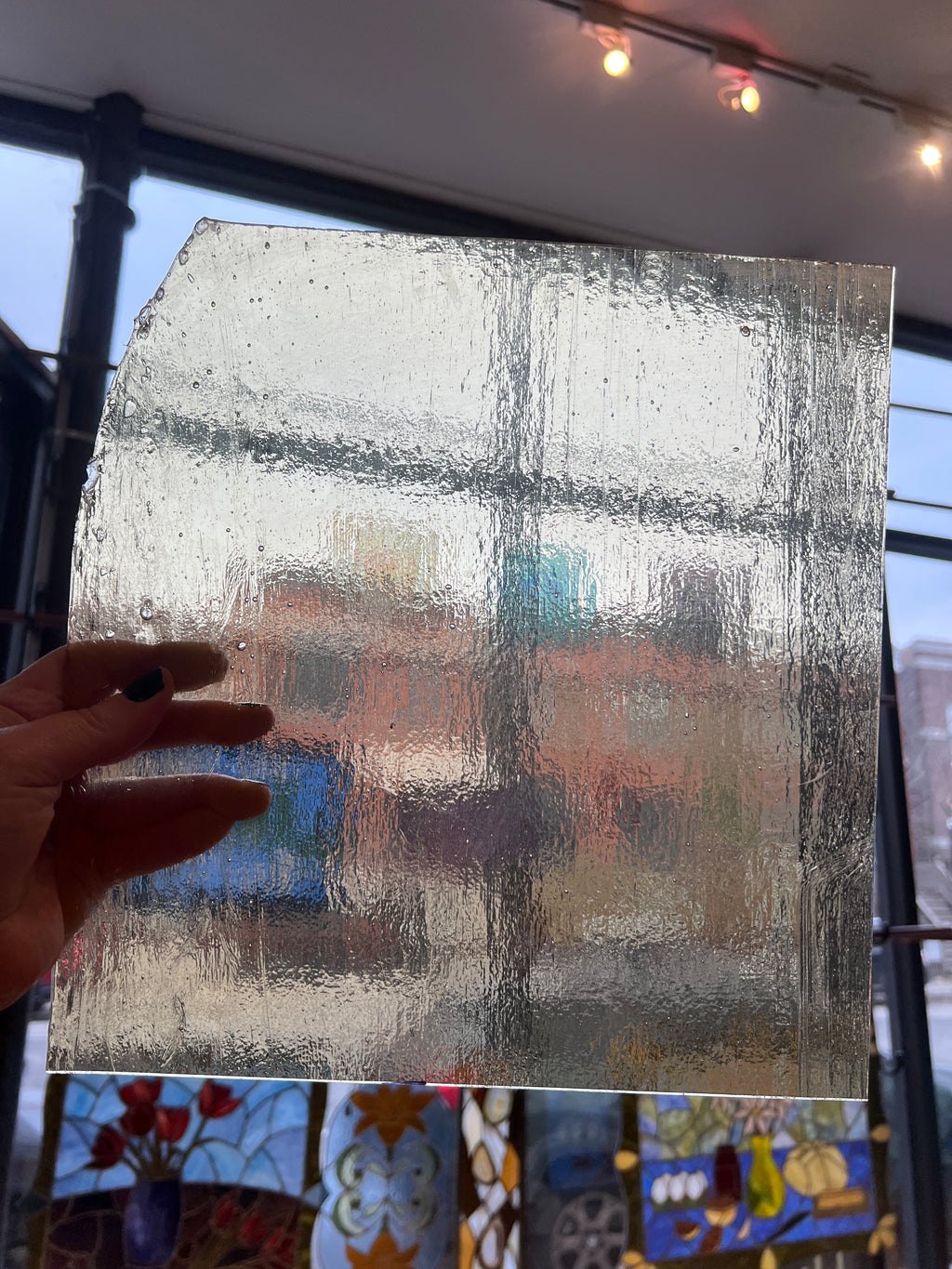 Hand holding a textured transparent sheet of glass with a blurred background