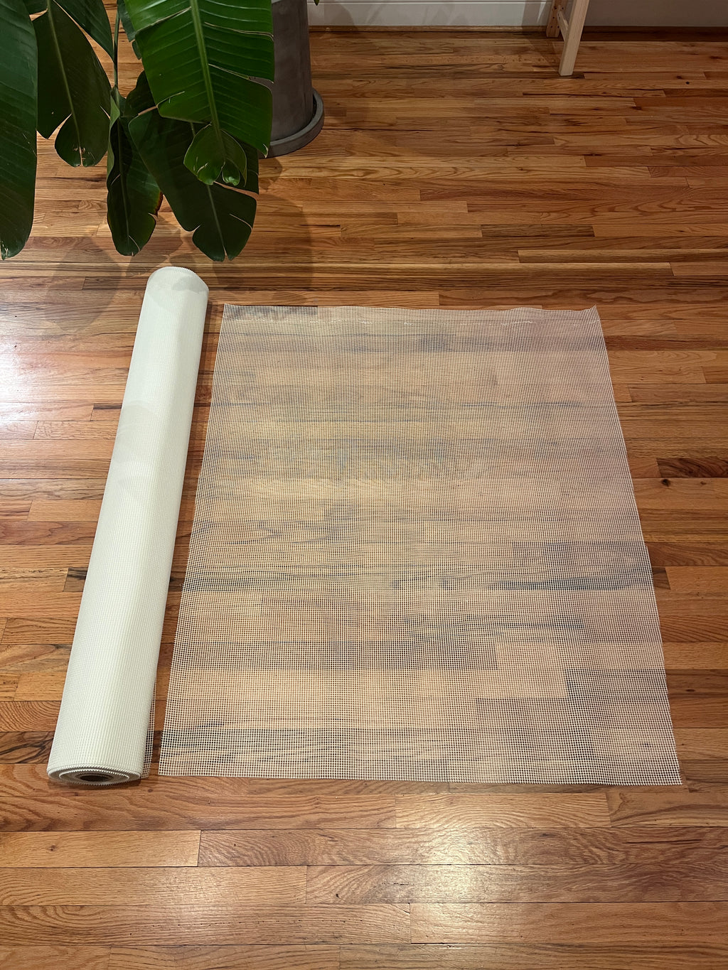 Roll of white mosaic mesh on a wooden floor with a plant in the corner